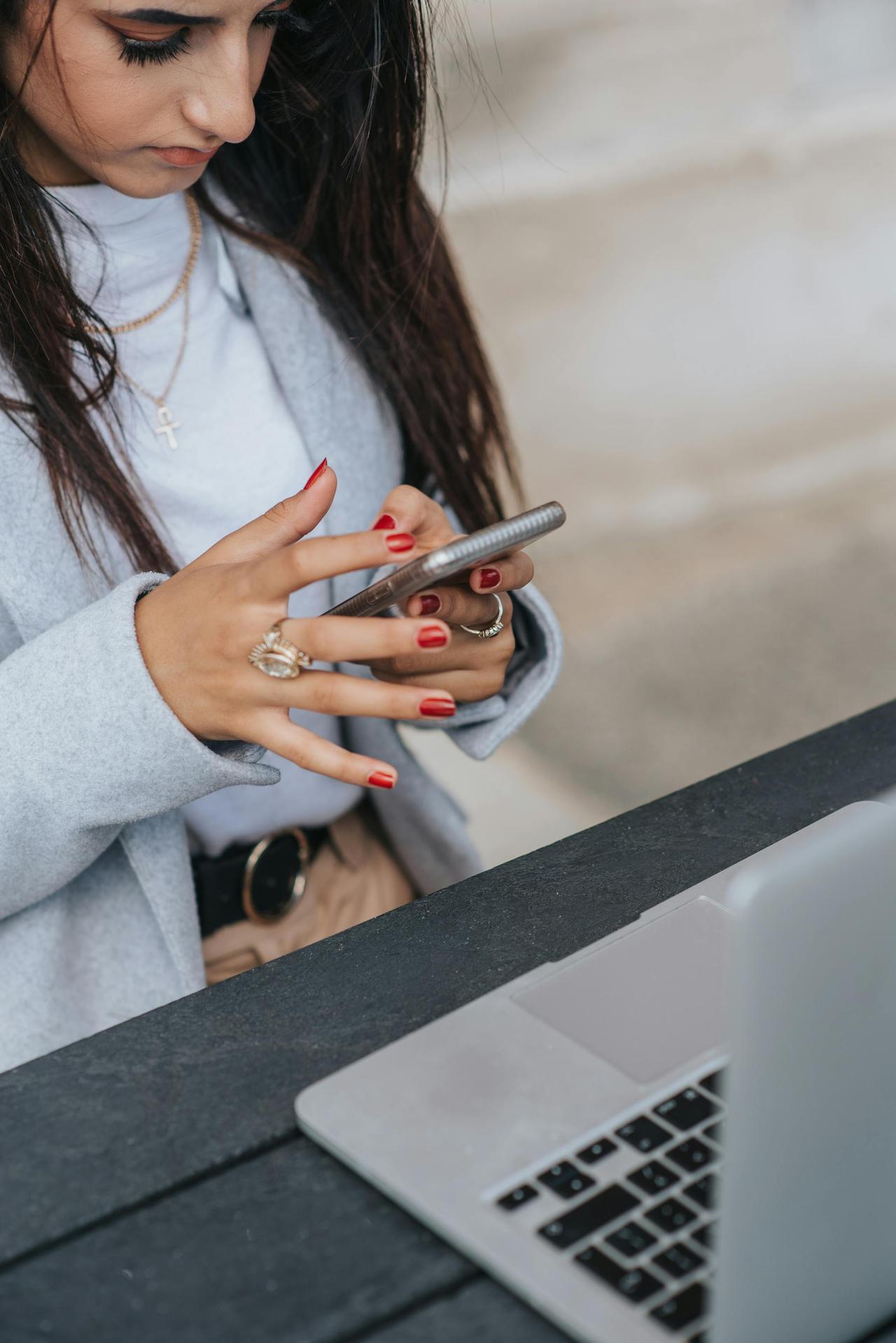Focused businesswoman texting on smartphone while working with laptop at an outdoor cafe table.