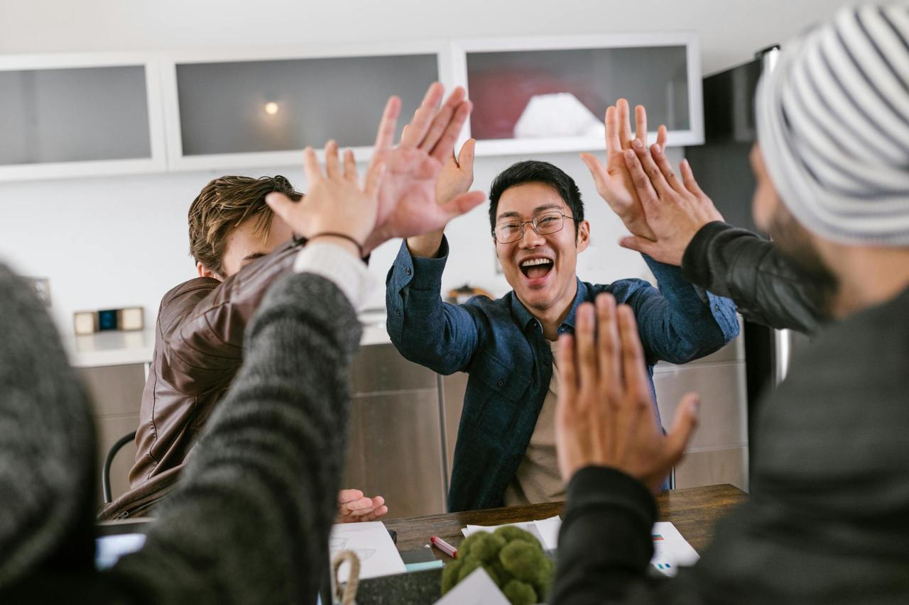 A group of diverse colleagues celebrate with a joyful high five at the office.