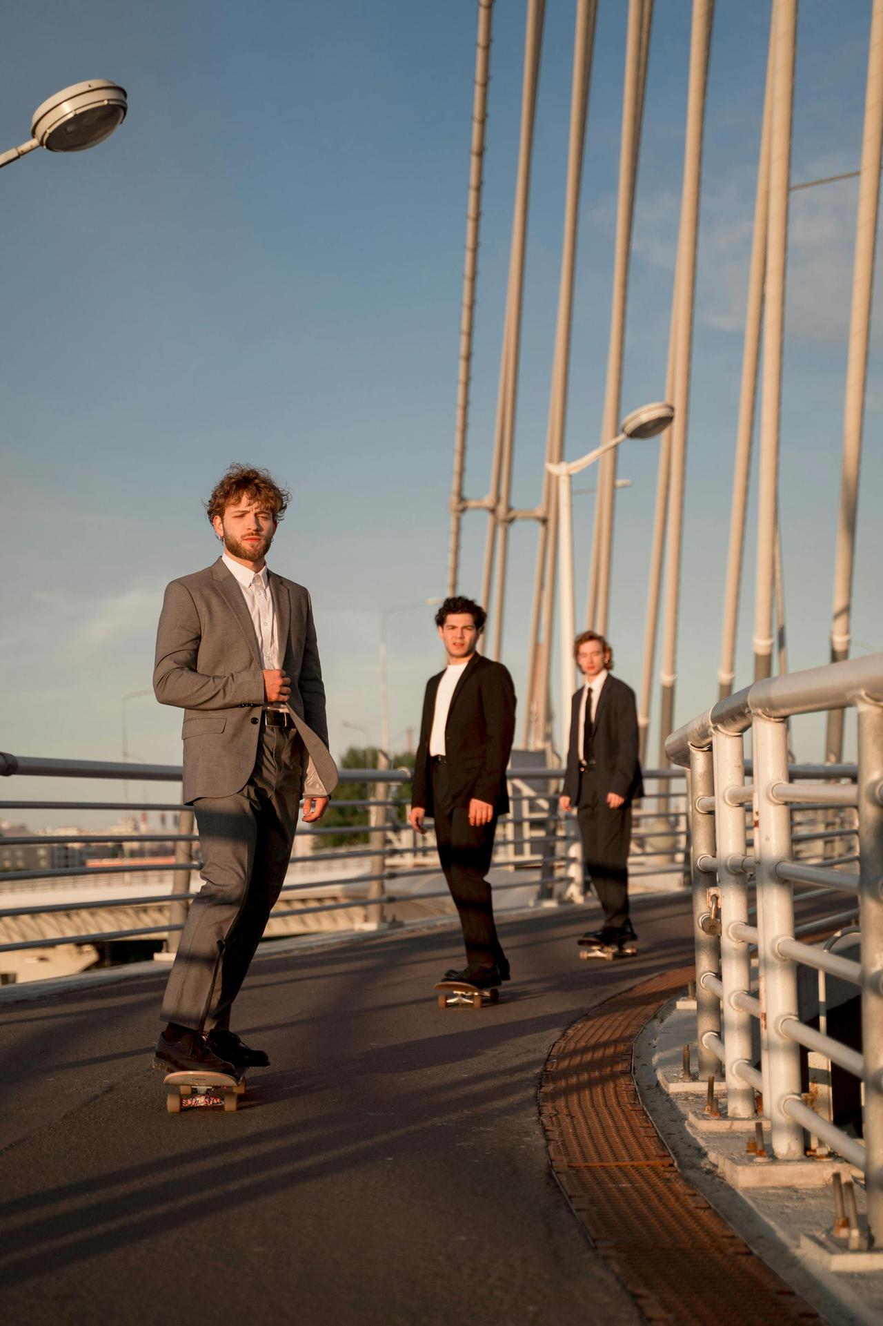 Three men in suits skateboarding on a city bridge during daytime.