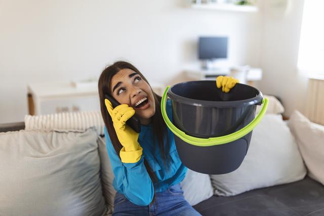 shocked-woman-calling-plumber-while-collecting-water-leaking-from-ceiling-using-utensil.jpg