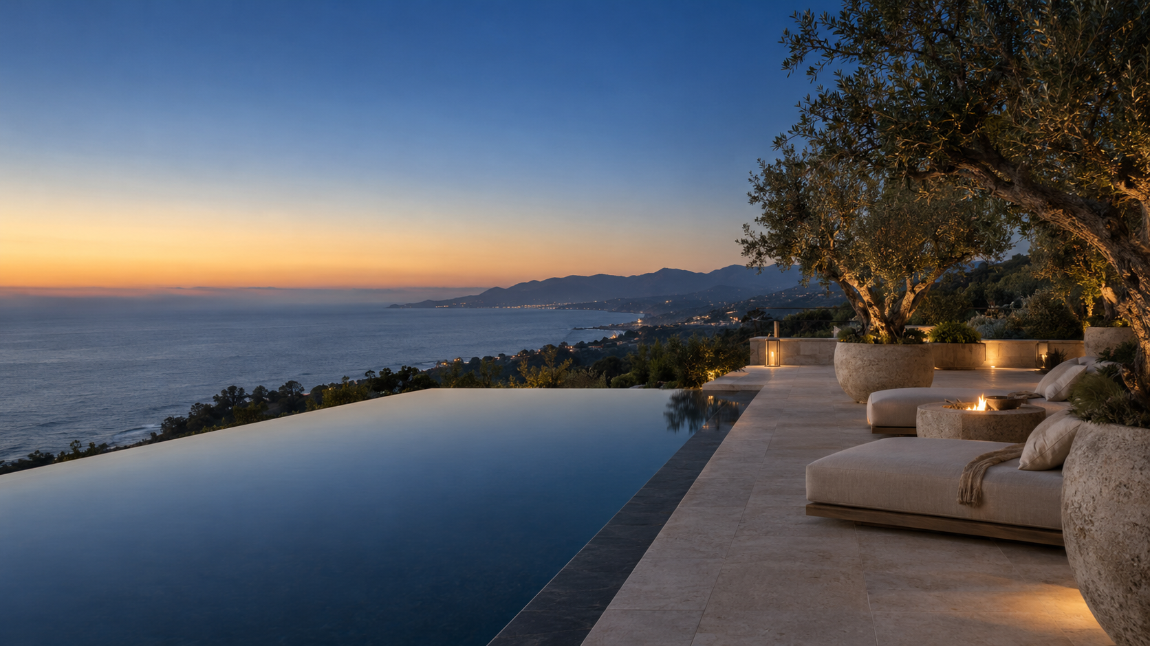 Montecito estate terrace at dusk: an infinity pool falling toward the Pacific, olive trees and stone loungers along the edge