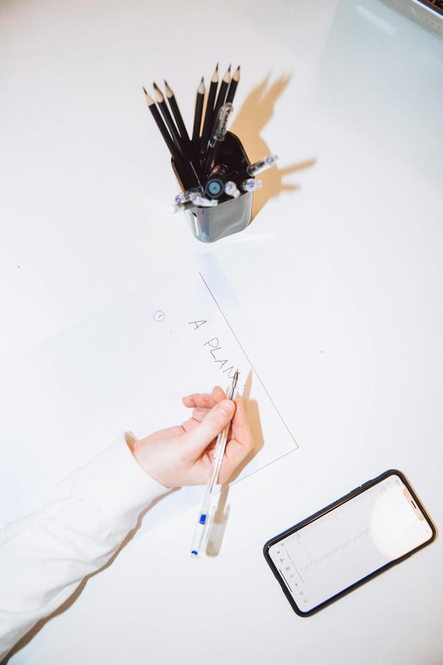 An overhead view of a woman planning on paper with a smartphone and pencils at a desk.