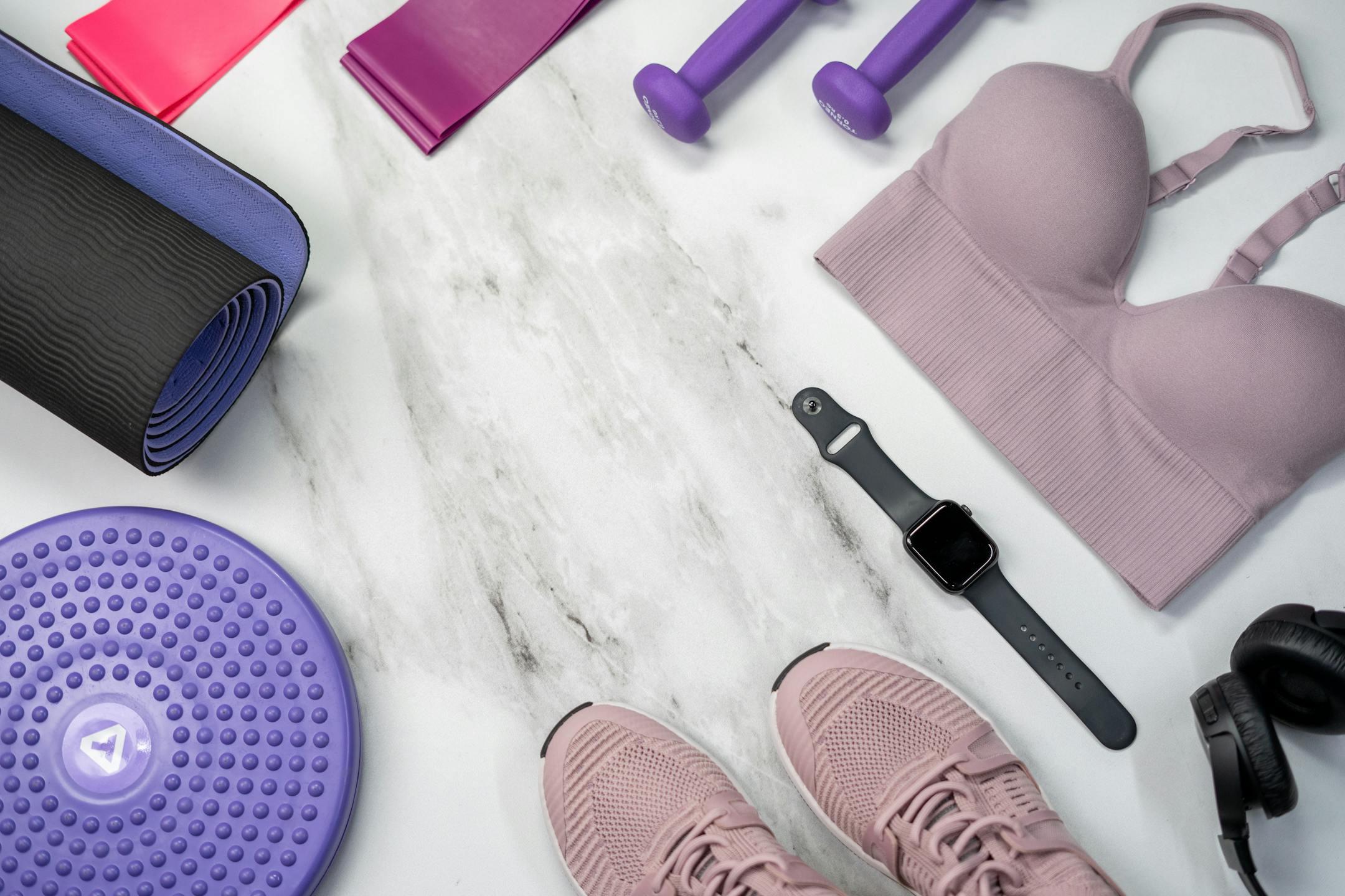 Top view of fitness equipment including smartwatch, bra, sneakers, and more on marble