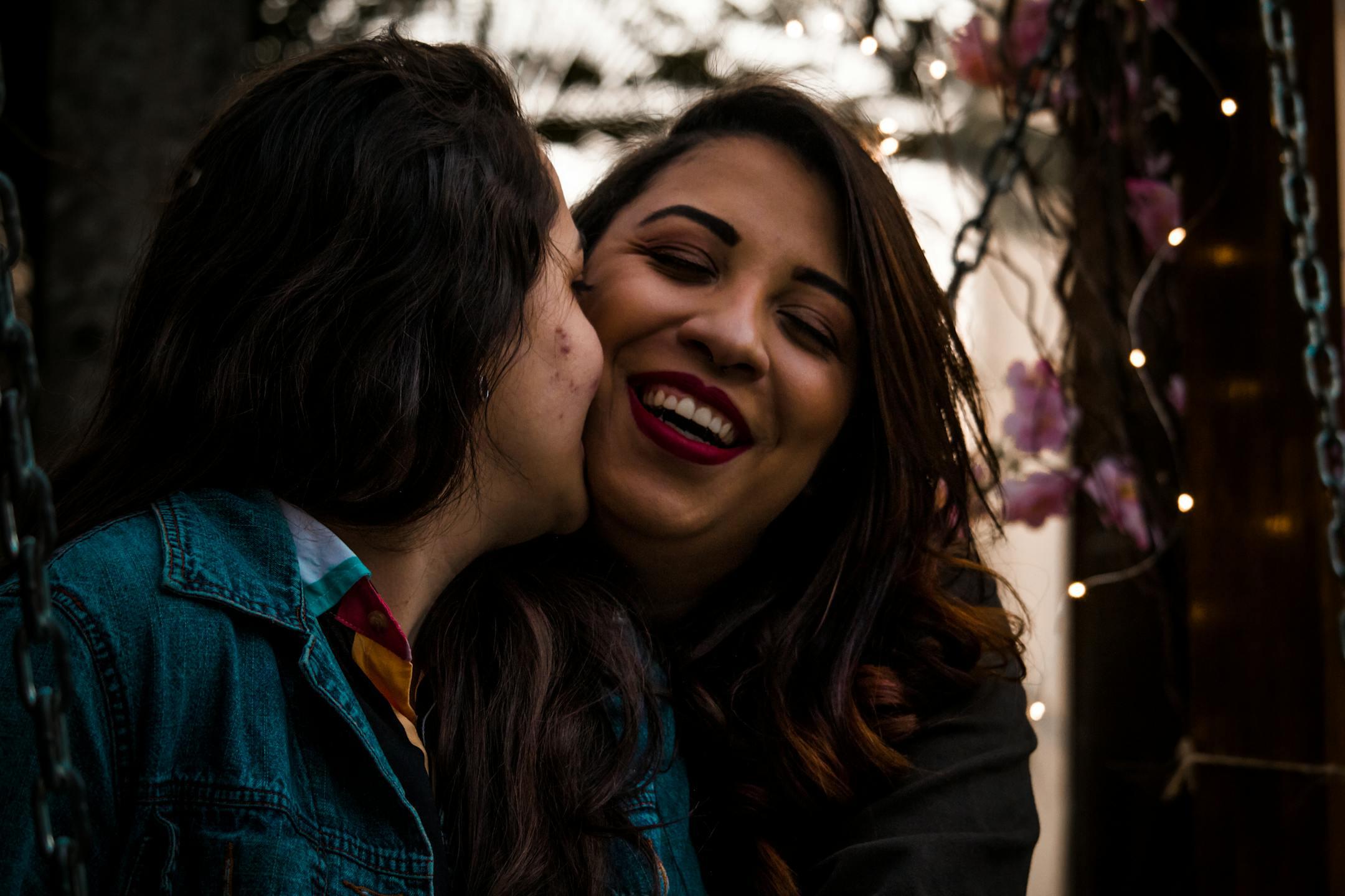 Happy LGBTQ couple smiling and enjoying a close moment outdoors, featuring colorful lights.