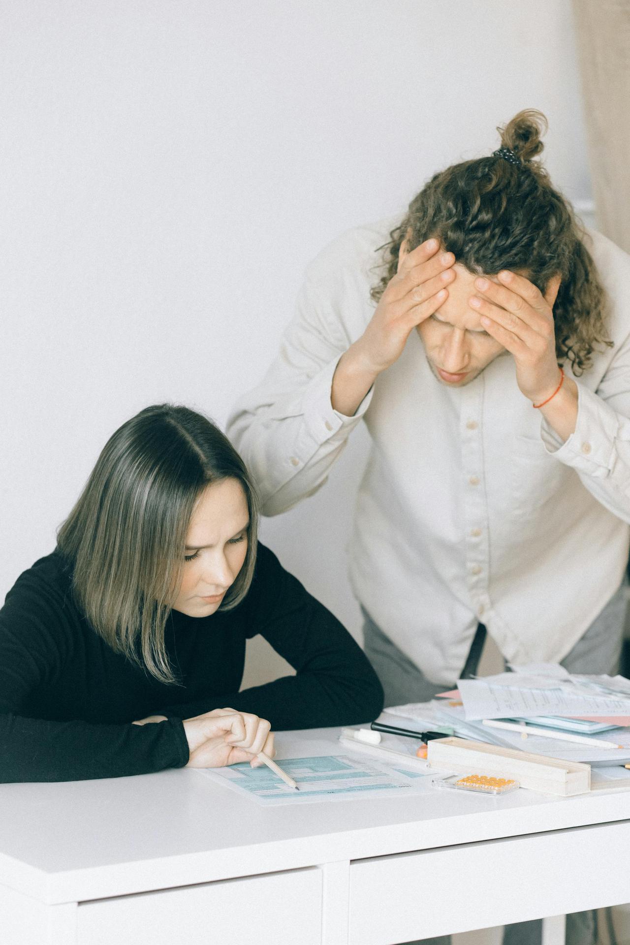 Young couple in discussion over financial papers, looking stressed at a table indoors.