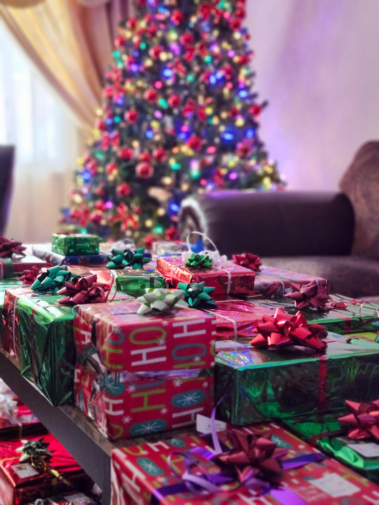 A vibrant Christmas tree and neatly wrapped presents create a festive indoor scene.