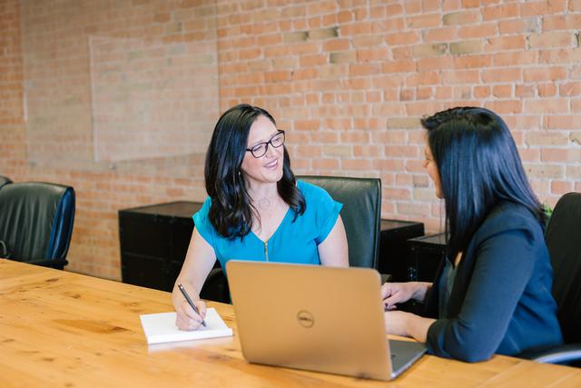 A woman speaking with another woman in front of a laptop.
