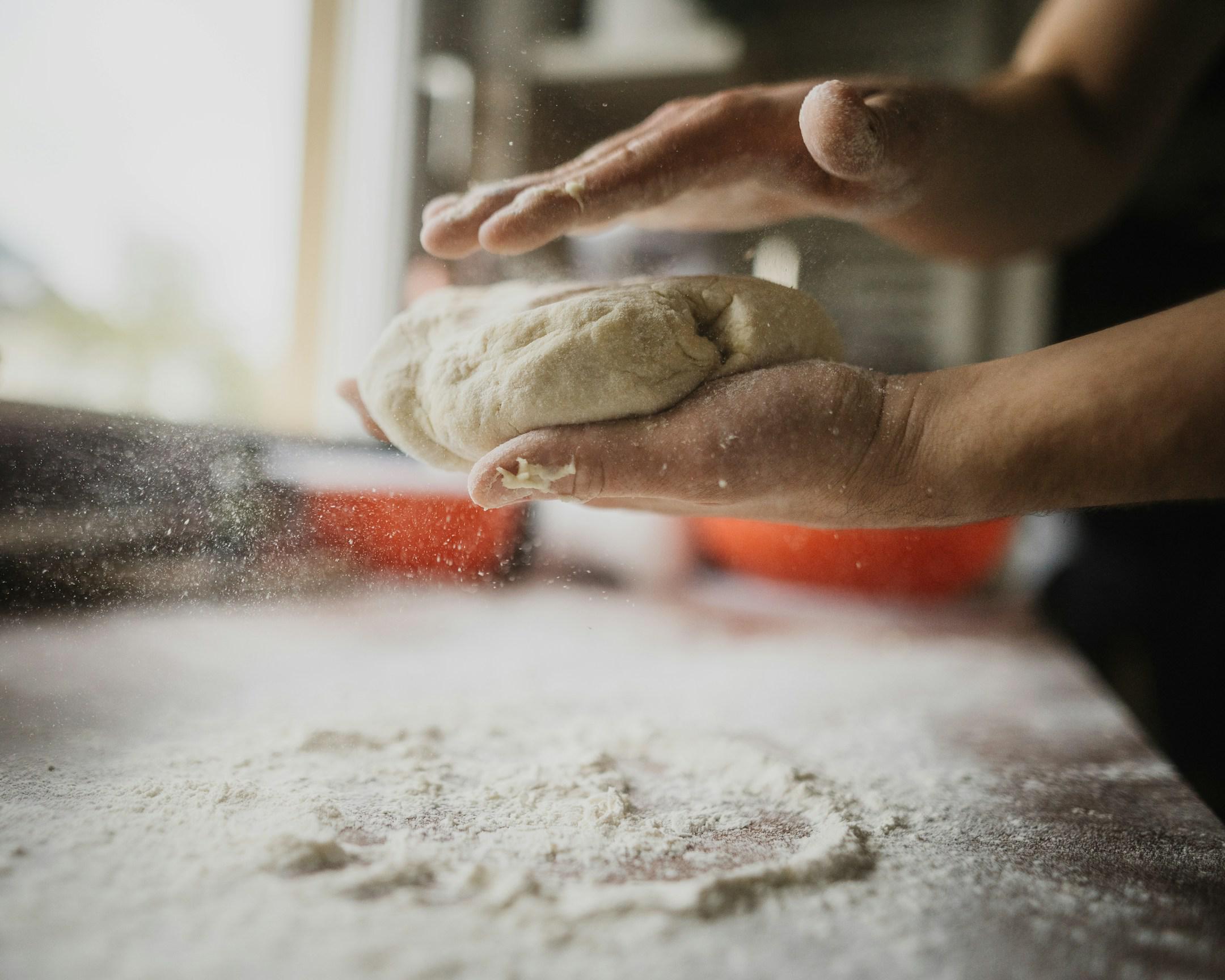 A person makes pizza dough with the hands. You can see some particles of flour in the air.