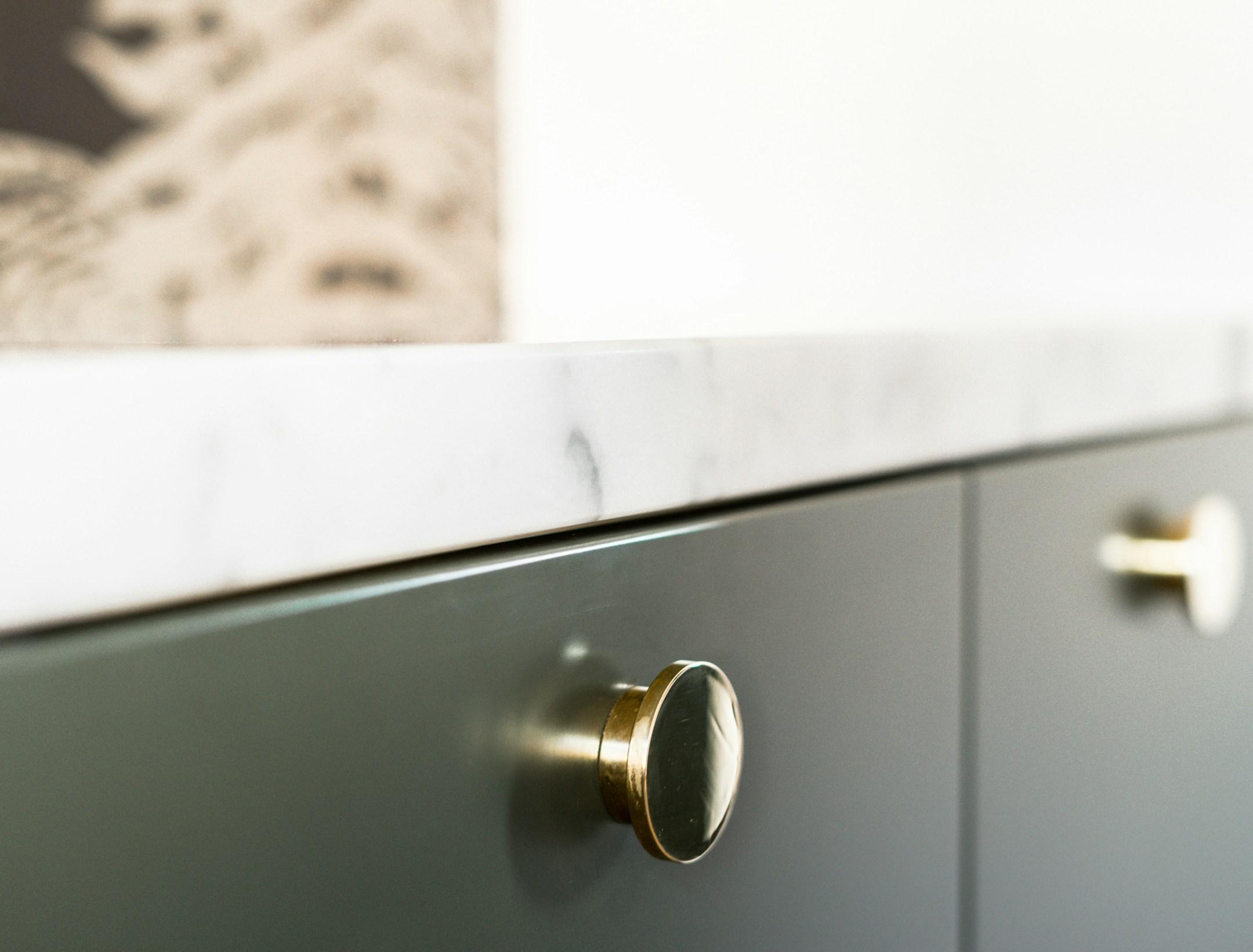 Brass knob on green kitchen front with marble countertop.