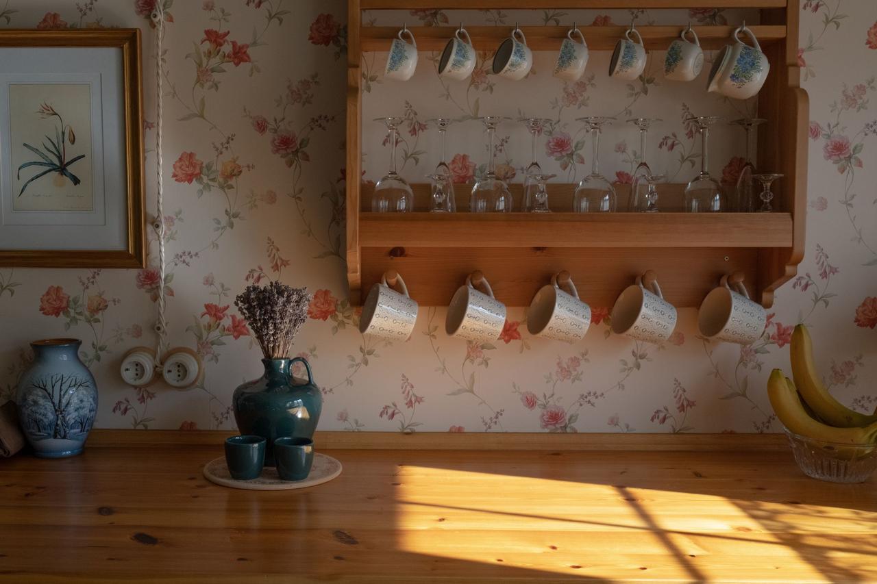 Vintage kitchen scene with floral mugs on a wooden shelf, sunlight casting warm shadows.