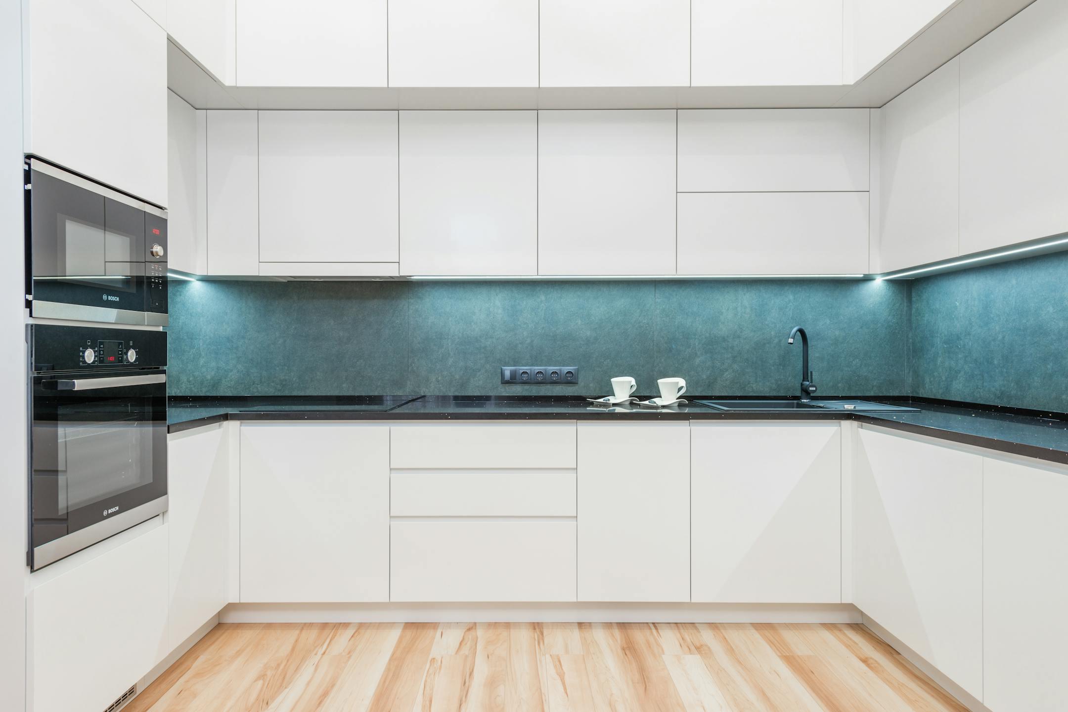Interior of white modern kitchen with minimalist design of white cabinets blue backsplash and black built in appliances