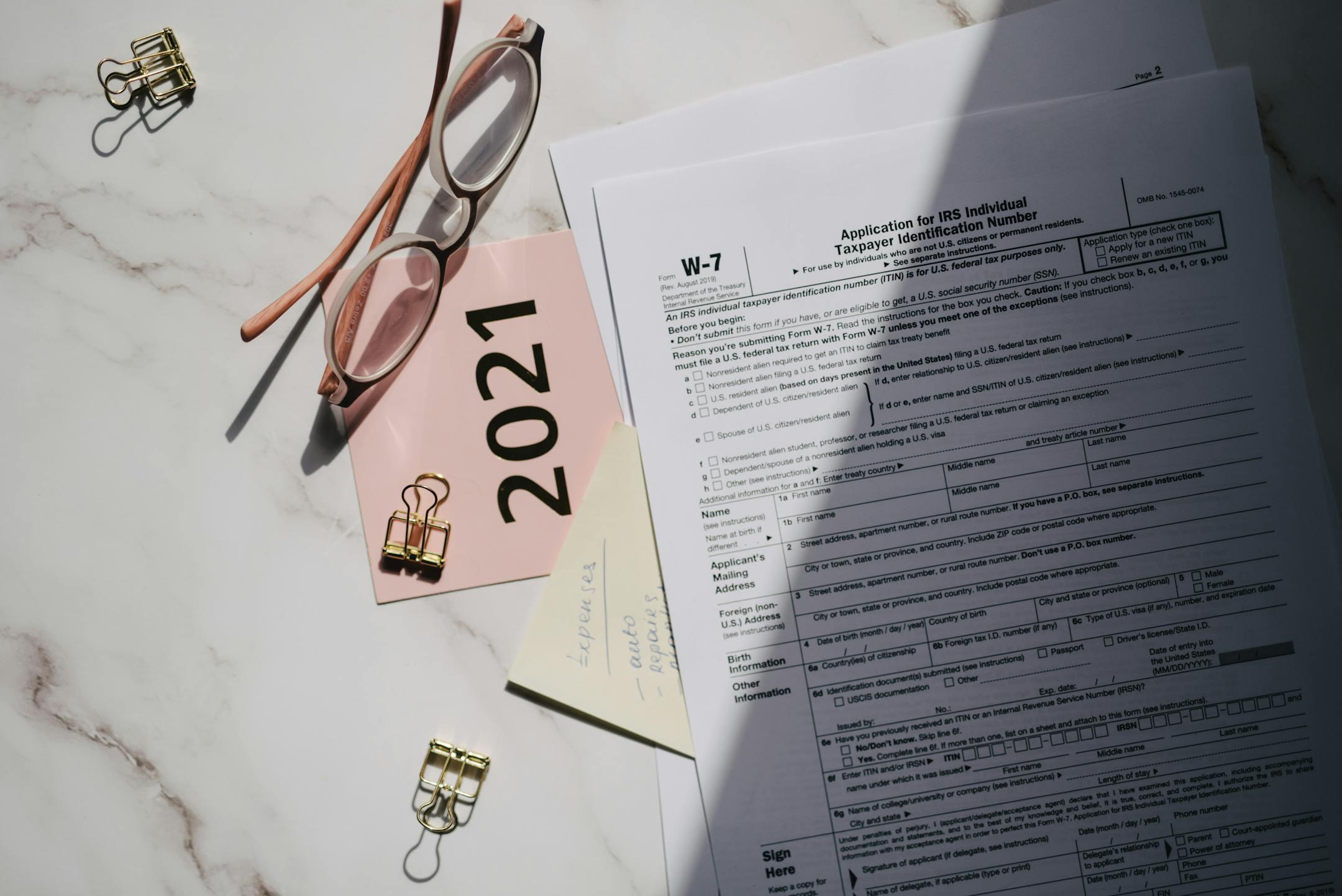Flat lay of IRS tax documents with reading glasses and 2021 note on a marble surface.