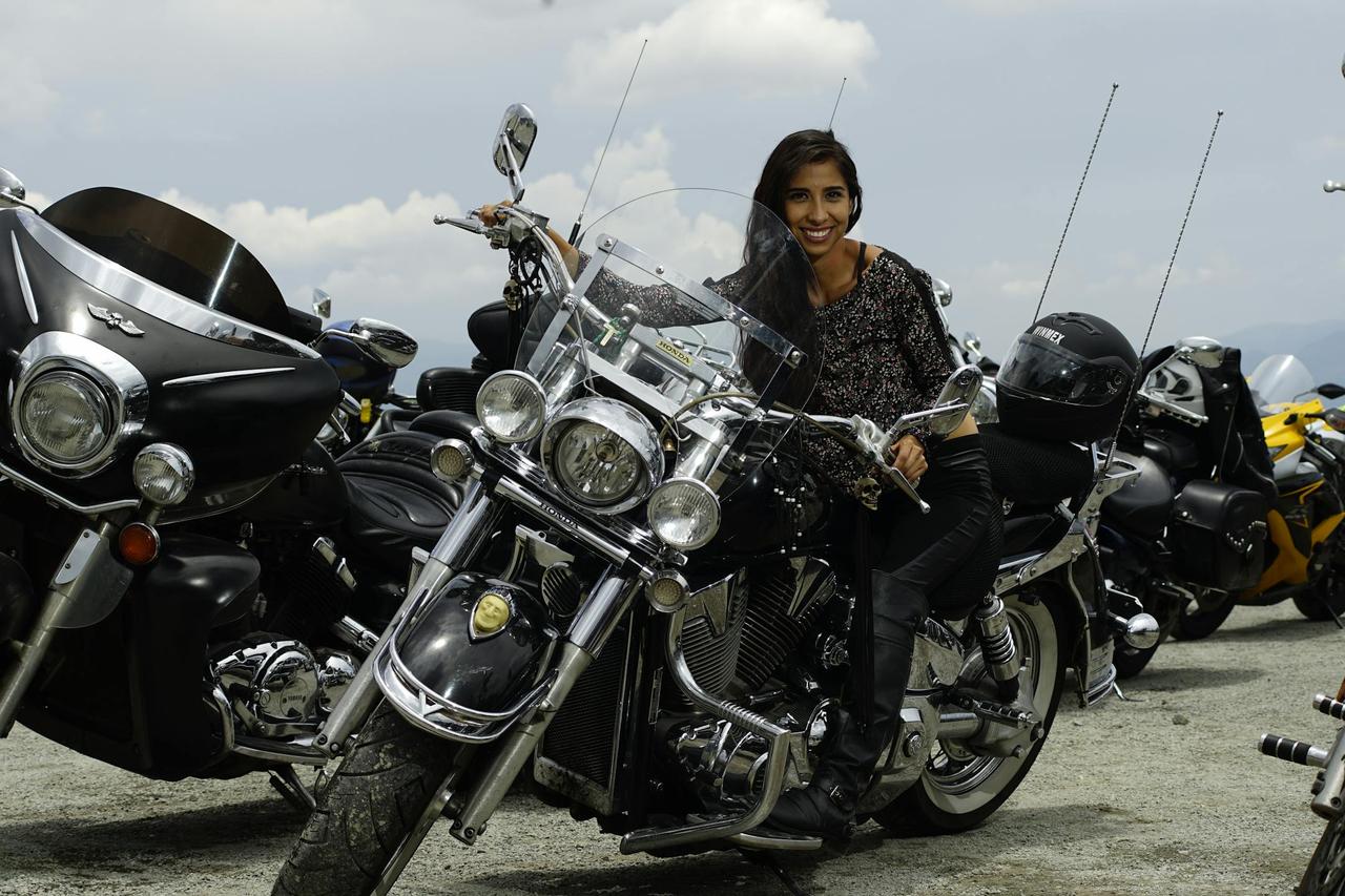 Smiling woman on motorcycle at an outdoor bike gathering with clear skies.