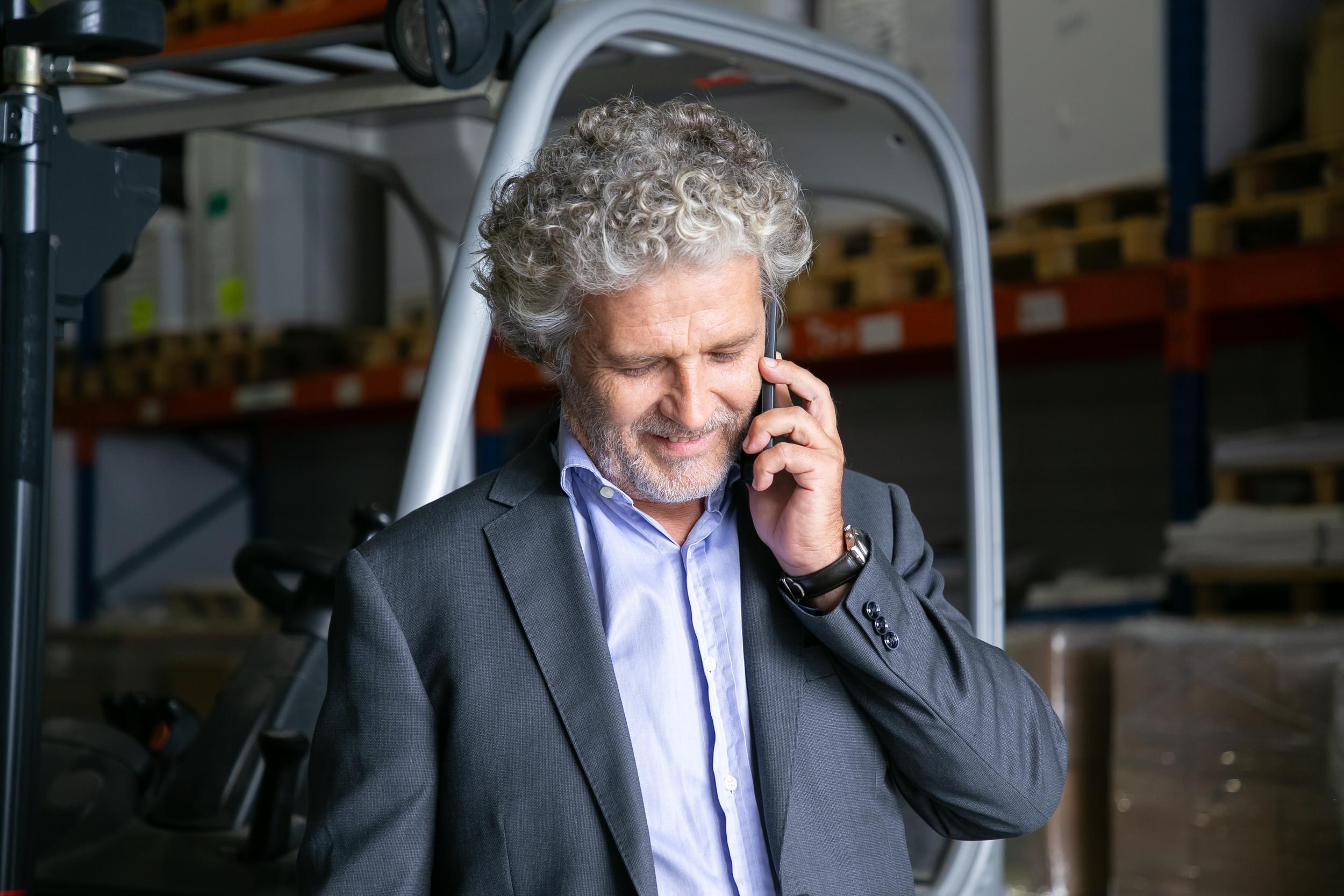 positive-businessman-standing-near-forklift-warehouse-talking-cellphone-shelves-with-goods-background-business-logistics-concept.jpg