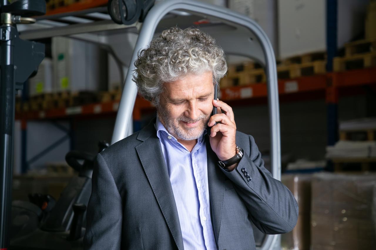 positive-businessman-standing-near-forklift-warehouse-talking-cellphone-shelves-with-goods-background-business-logistics-concept.jpg