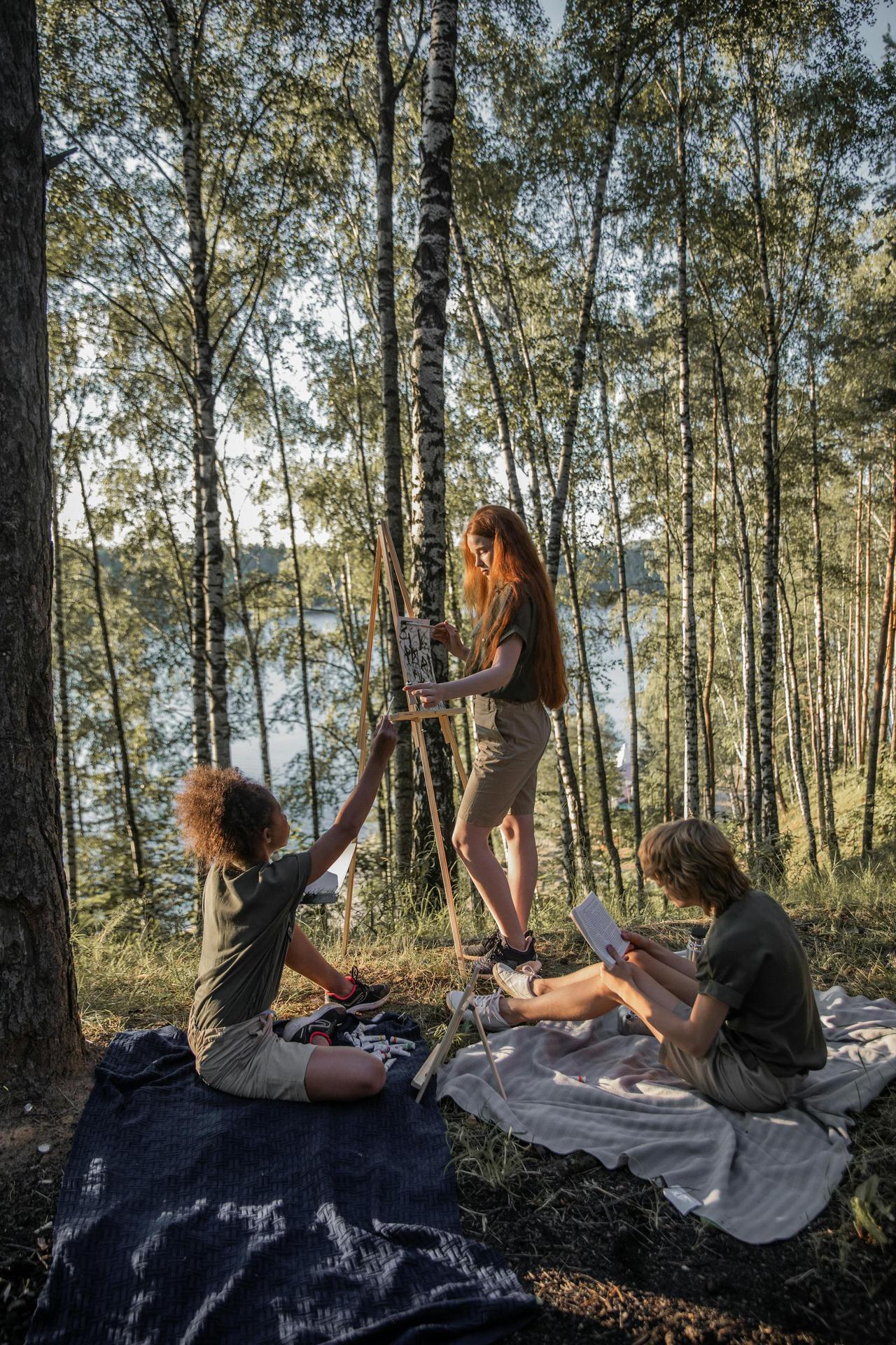 Children engage in plein air painting in a serene forest with trees and natural light.