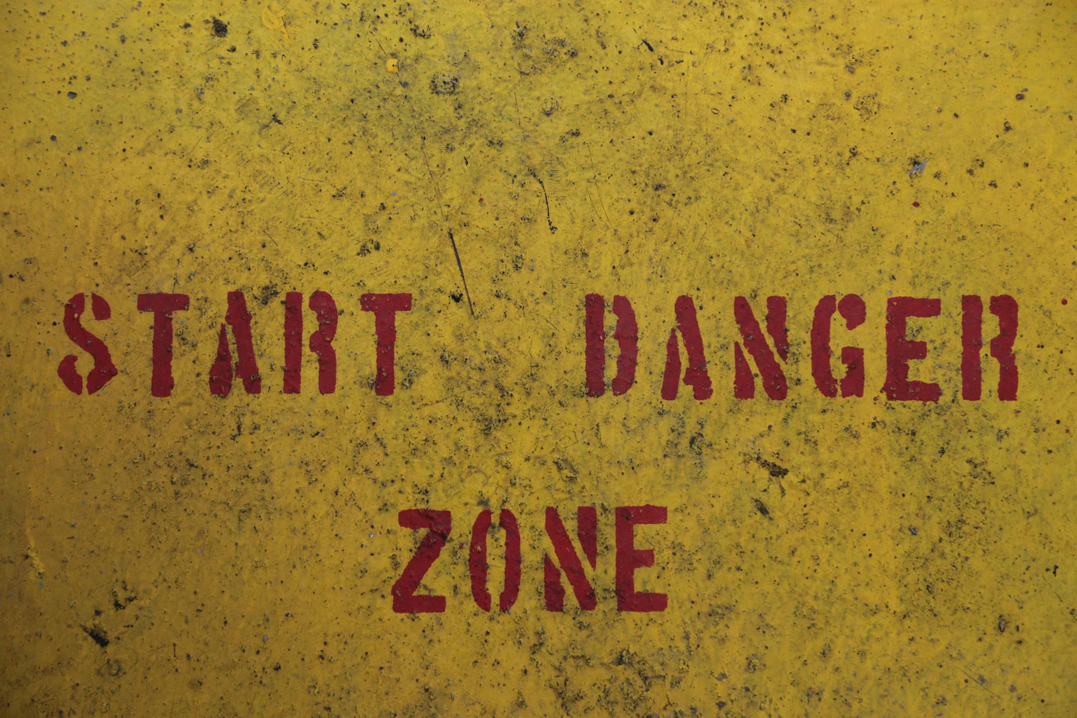 Warning text on a Container Vessel This image captures the essence of caution with 'START DANGER ZONE' boldly painted in red on a textured yellow surface. The gritty, worn look adds a sense of urgency and the necessity for awareness. It’s an illustrative example of industrial safety signage and its importance in hazardous environments.