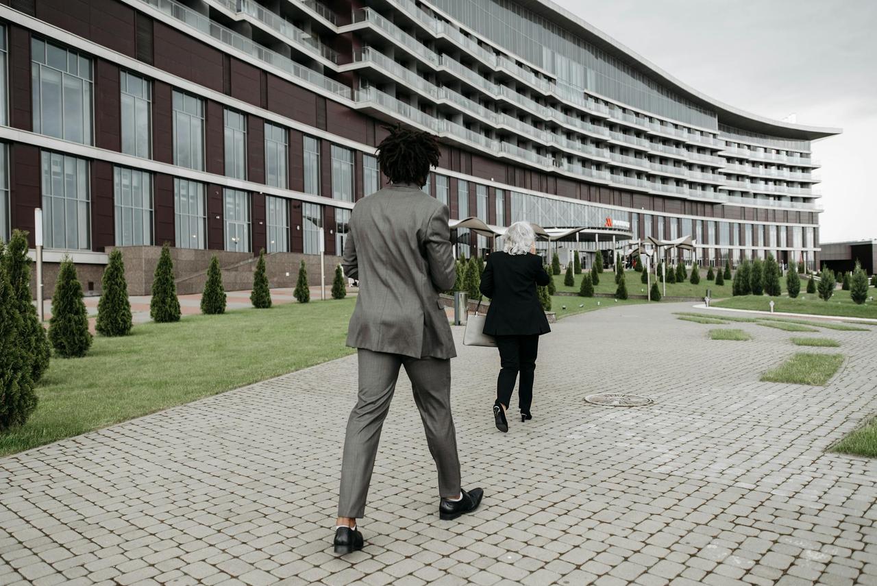 Two business professionals in formal attire walking outside a modern office building.