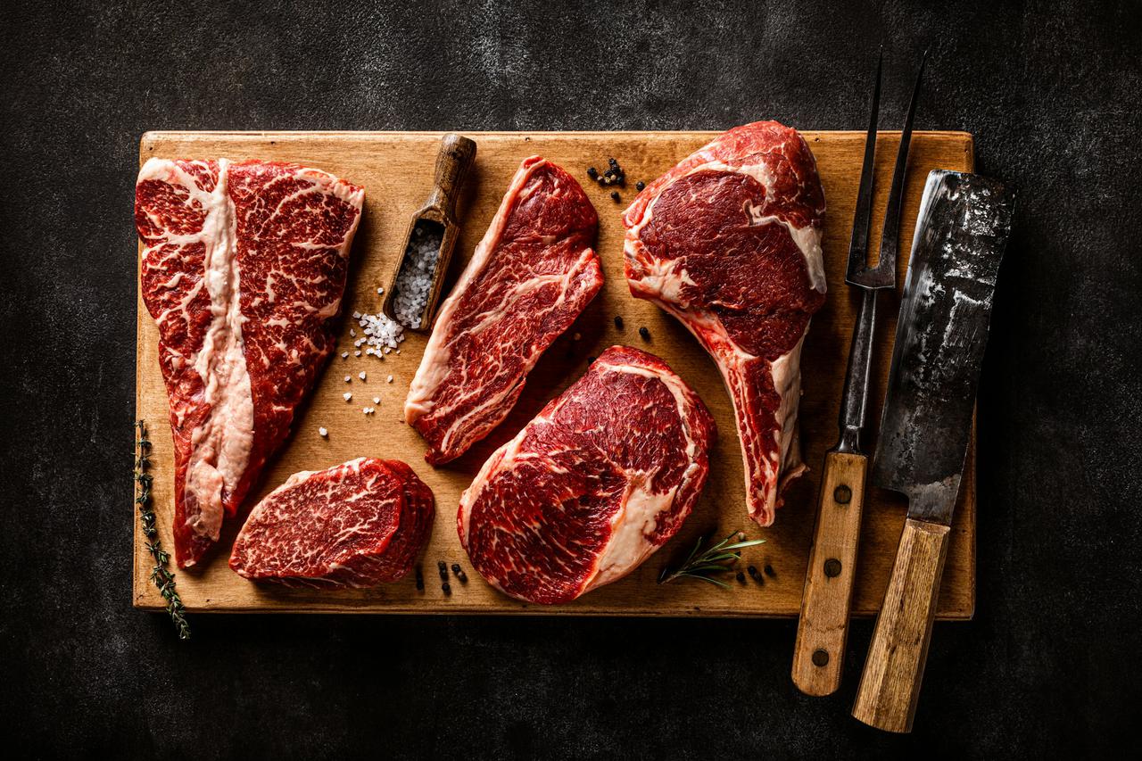 Assortment of raw meat cut with seasoning and utensils on wooden rustic board