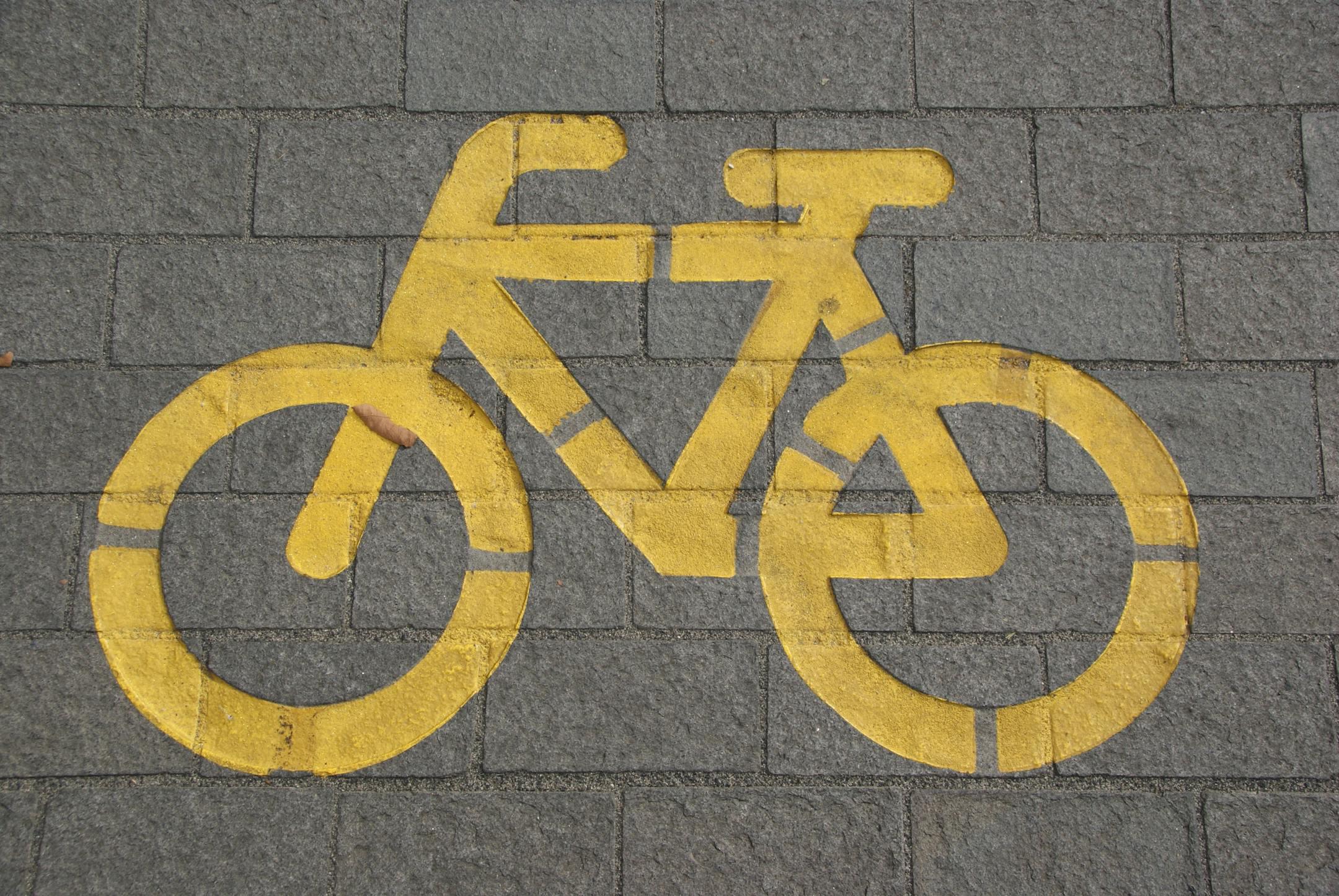 Bright yellow bicycle symbol on gray pavement marking a bike lane.