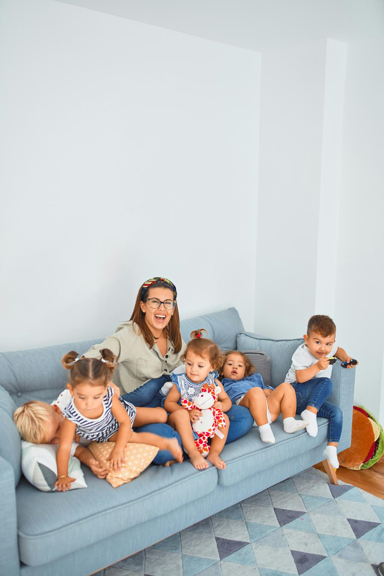 Beautiful teacher and group of toddlers sitting on the sofa playing at kindergarten