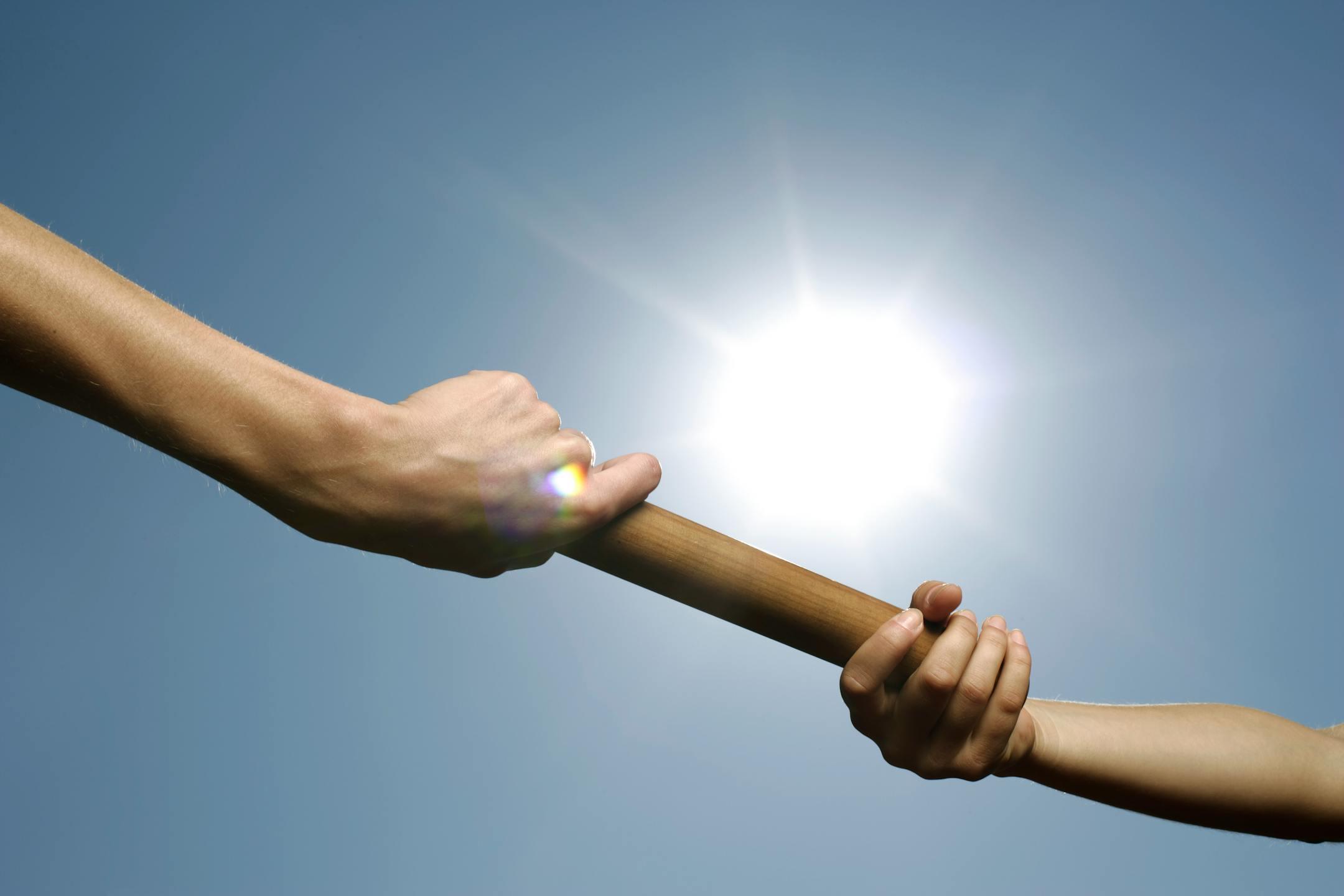 Close-up of hands passing a relay baton against a bright sunny sky.