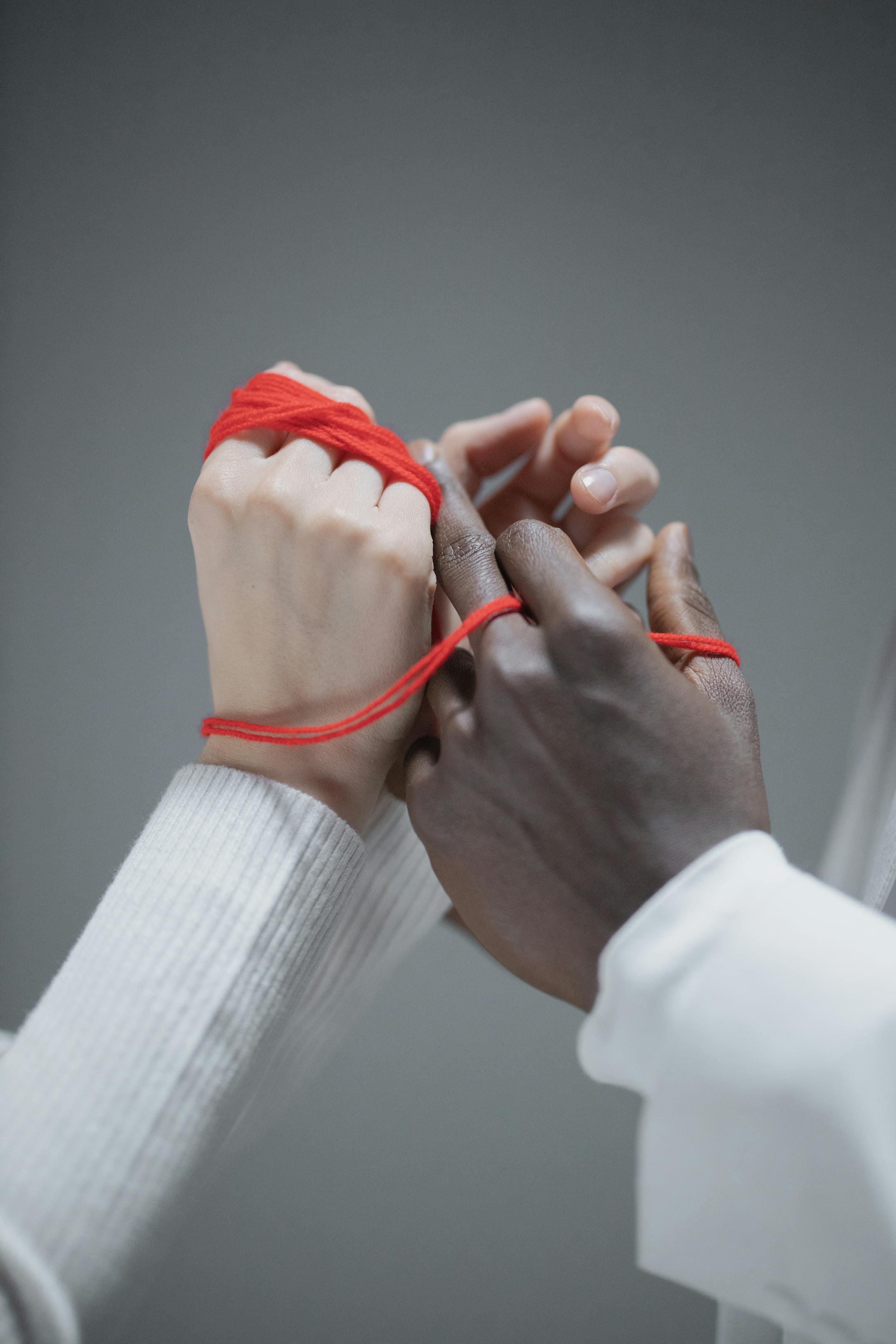 Two diverse hands wrapped with red string, symbolizing connection and diversity.