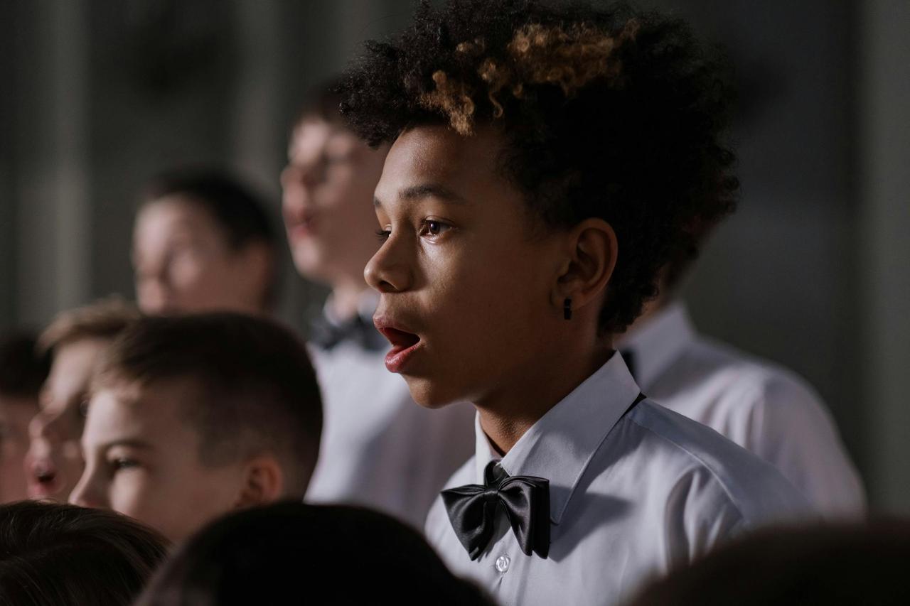 A group of boys in a choir singing passionately with focus on African American boy.