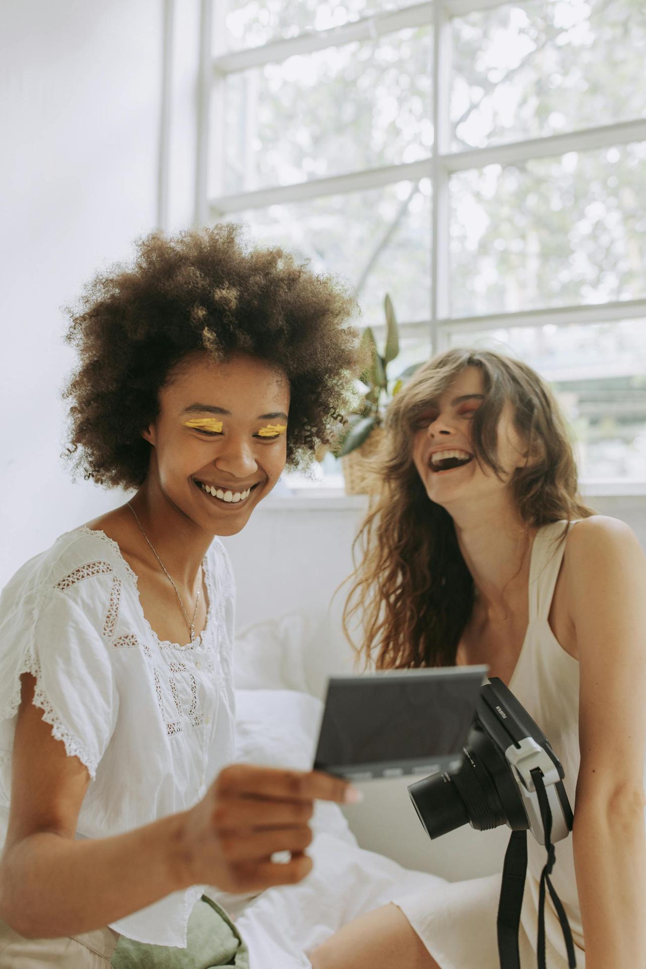 Two friends laughing while looking at instant photos on a sunny day.