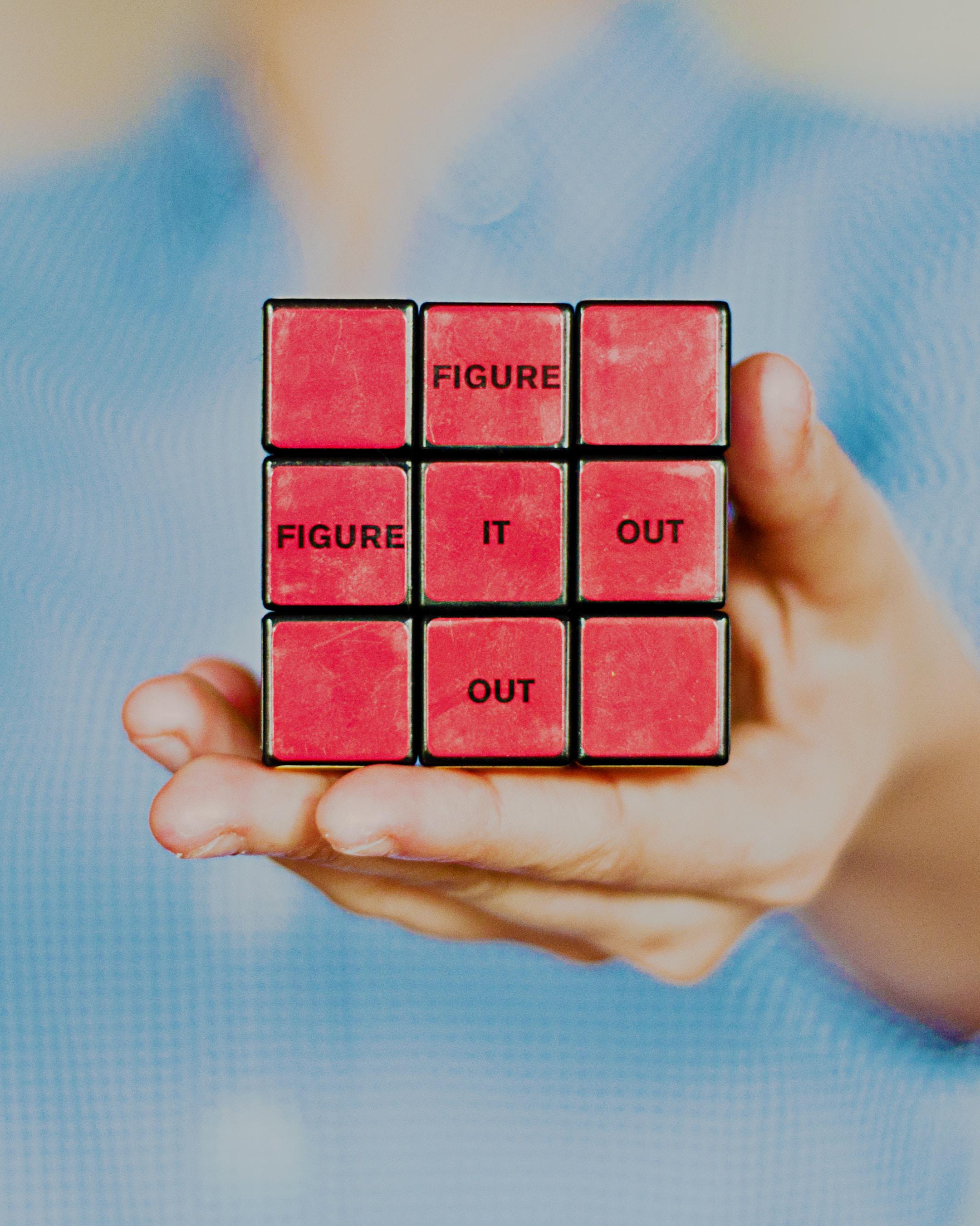 Person holding a solved rubik's cube with the words "figure it out".