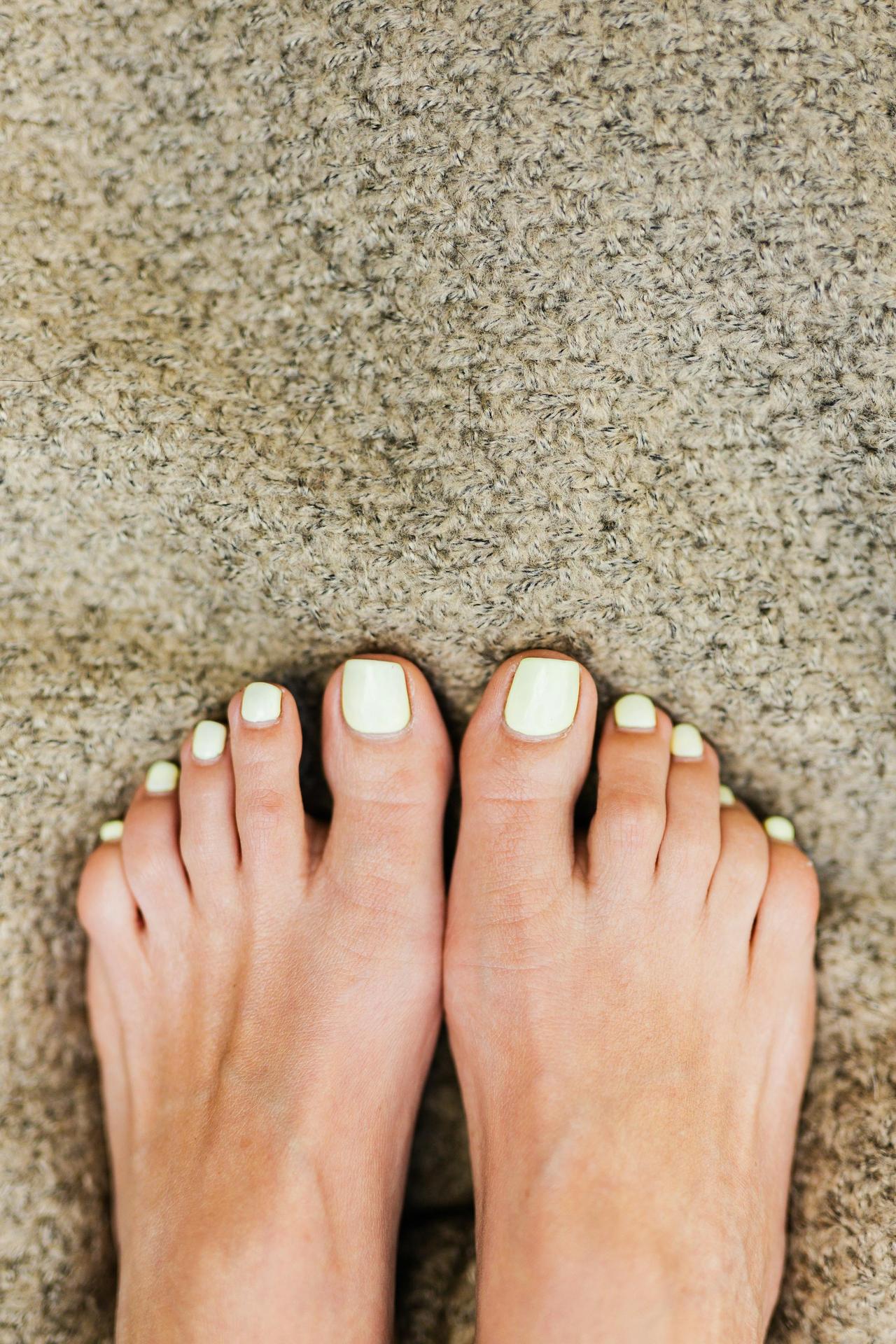 Close-up of bare feet with light green nails on a textured carpet.