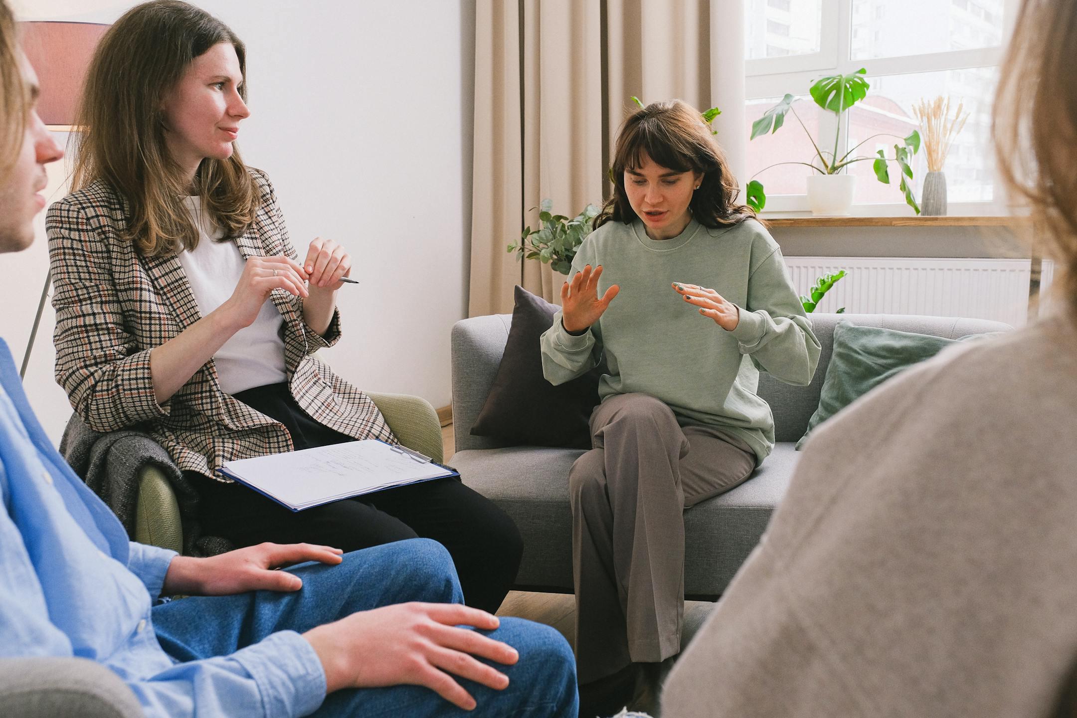 Women in casual clothes sitting on sofa and speaking during group psychotherapy session in cozy office