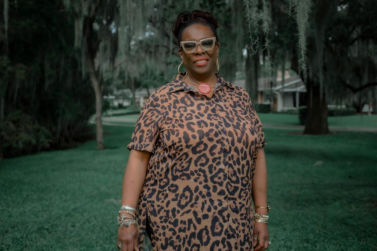 Confident woman in leopard print dress smiling in a lush green park setting.