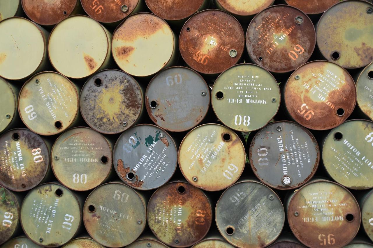 Pile of old, rusty oil barrels stacked outdoors with visible labels and numbers.