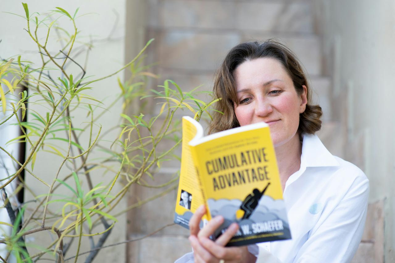 A woman in white shirt, sitting on the steps outside, reading a yellow paperback book - smiling