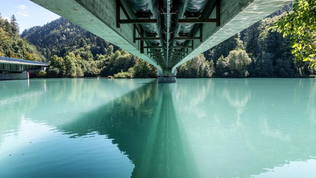 Stunning view under a bridge over a calm river surrounded by lush green forest in Füssen, Germany.