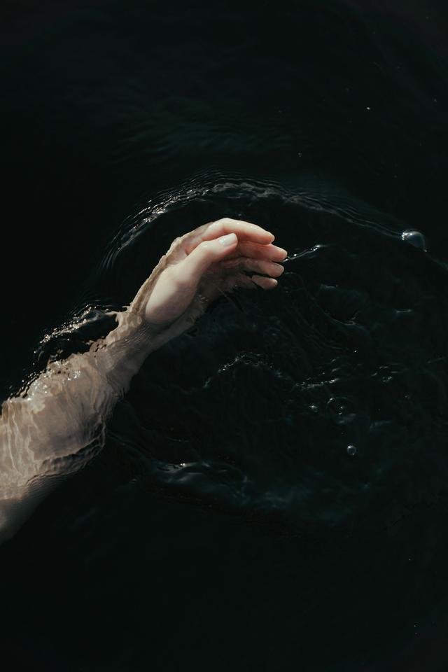 A serene hand gracefully touching the dark, mysterious water surface, creating ripples.