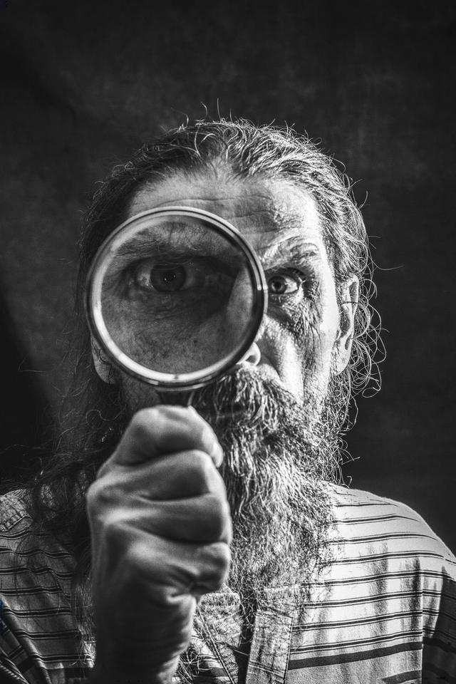 Black and white portrait of a bearded man using a magnifying glass for inspection.