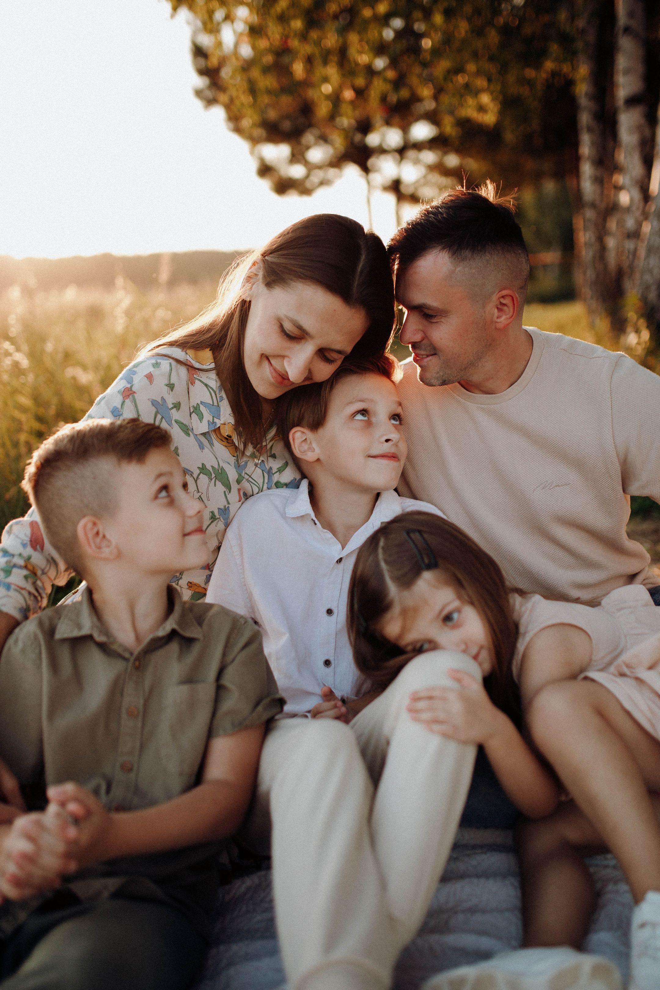 A joyful family of five sitting together, enjoying a warm sunset in the countryside.