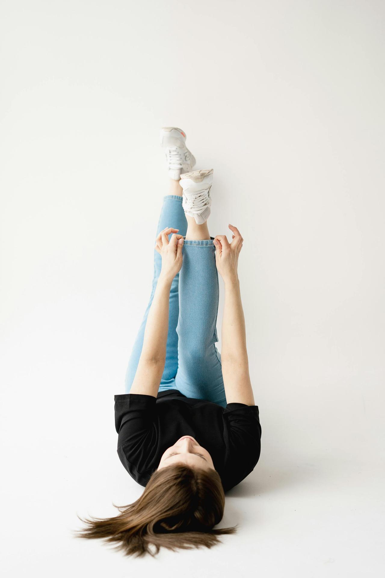 A woman in jeans and a t-shirt lying upside down with legs raised, posing casually.