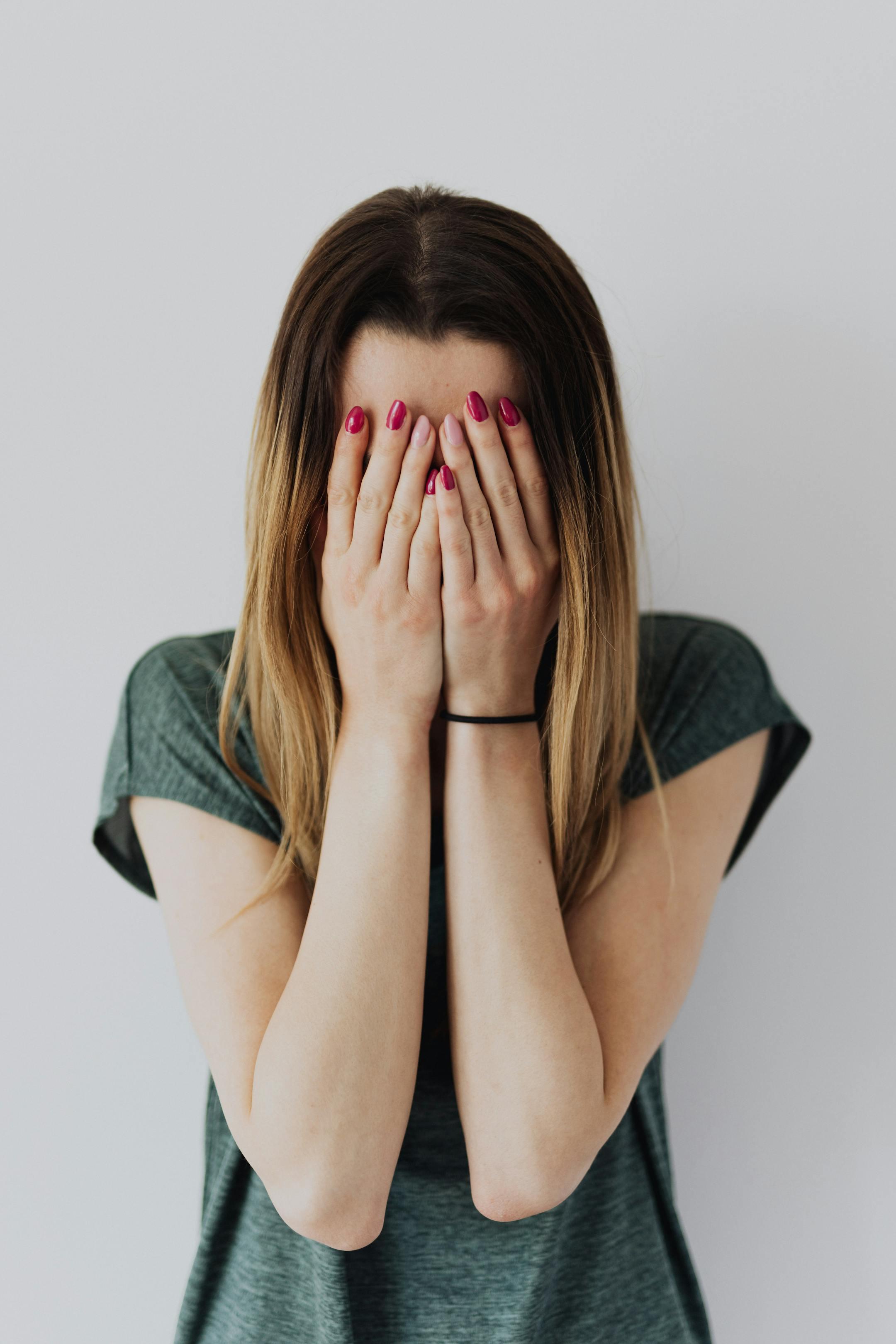 A young woman covers her face with her hands in an expression of fear and anxiety.