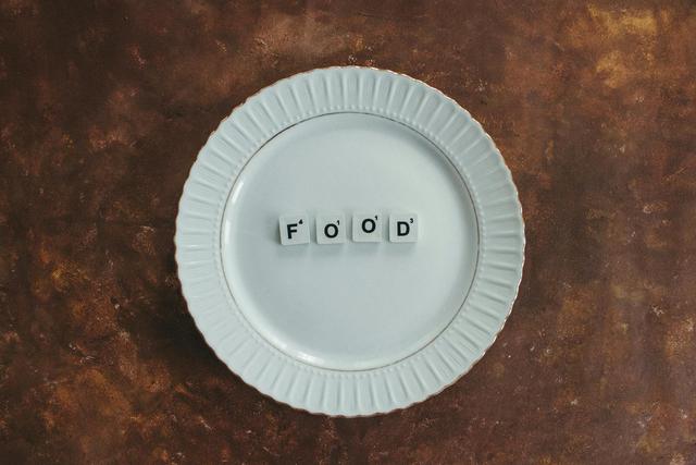 A minimalist composition featuring a white plate with the word 'food' in scrabble tiles on a textured background.