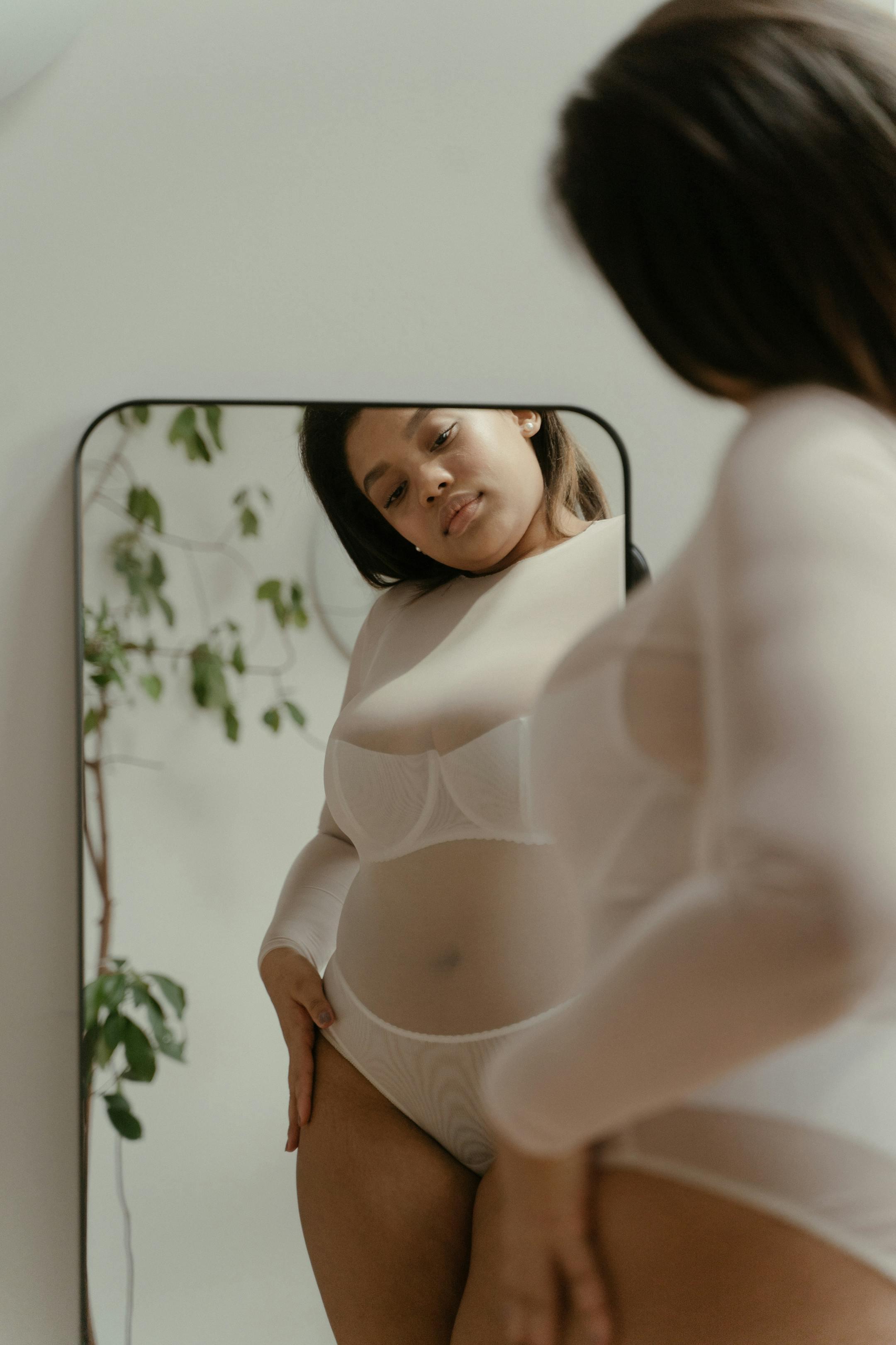 A woman embraces self-love and body positivity in a reflective mirror portrait.