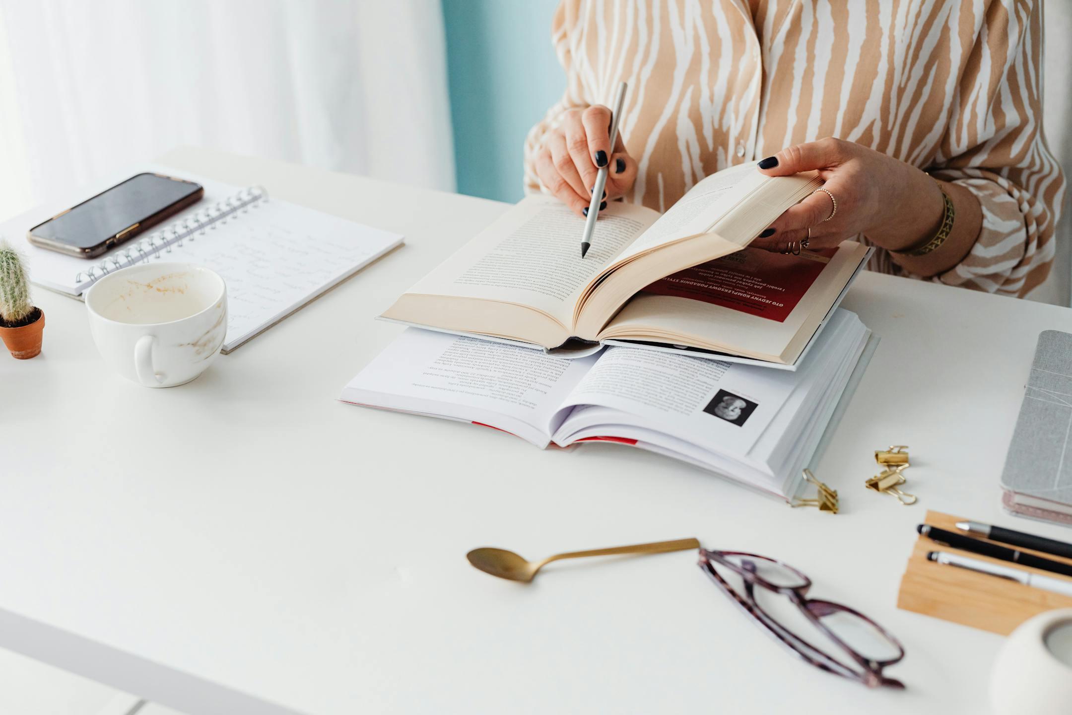 Woman reading and taking notes at a desk with books, notebook, and coffee