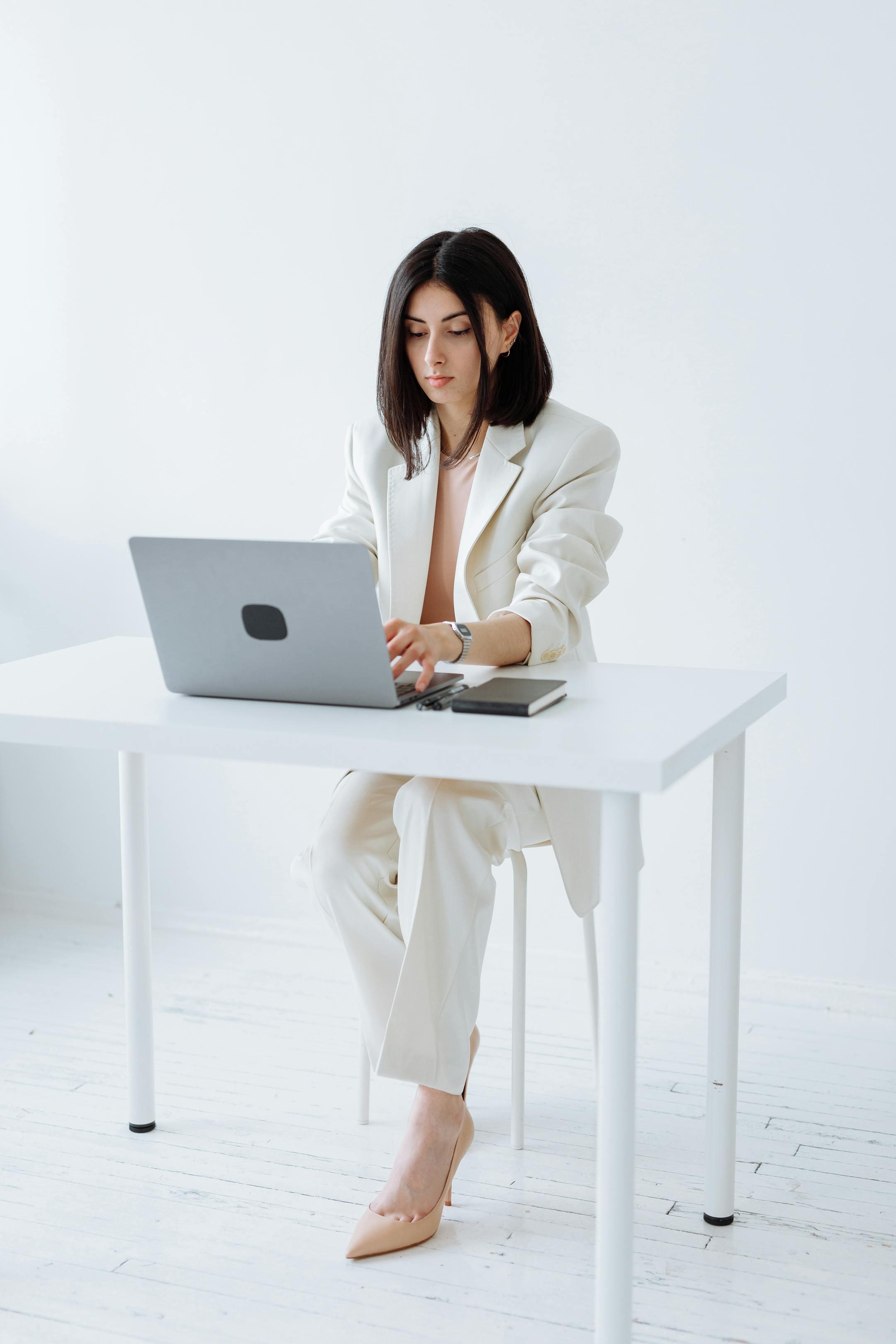 Businesswoman in a white suit working on a laptop in a minimalist office setting.