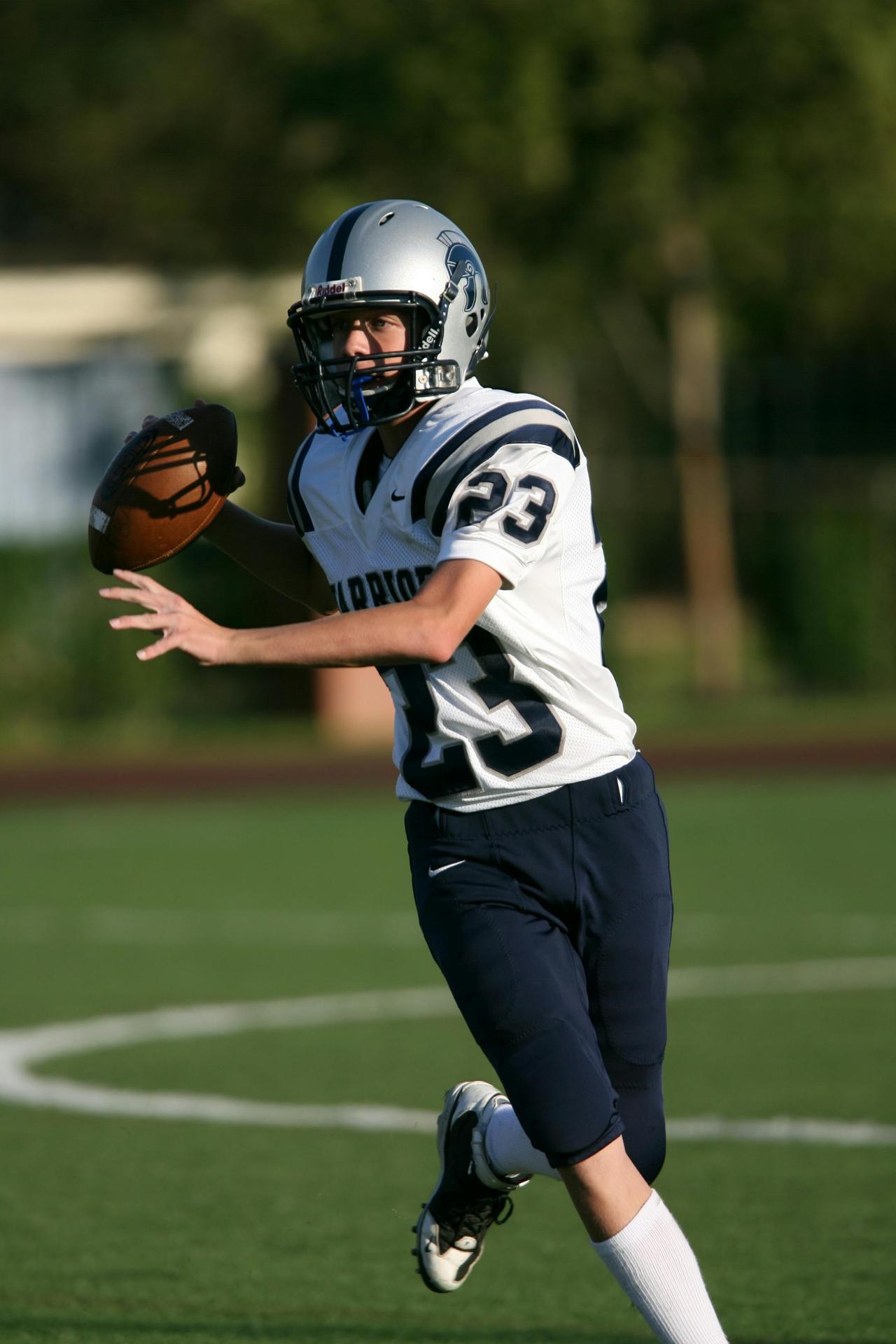 Teen football quarterback in uniform making a pass during a game outdoors.