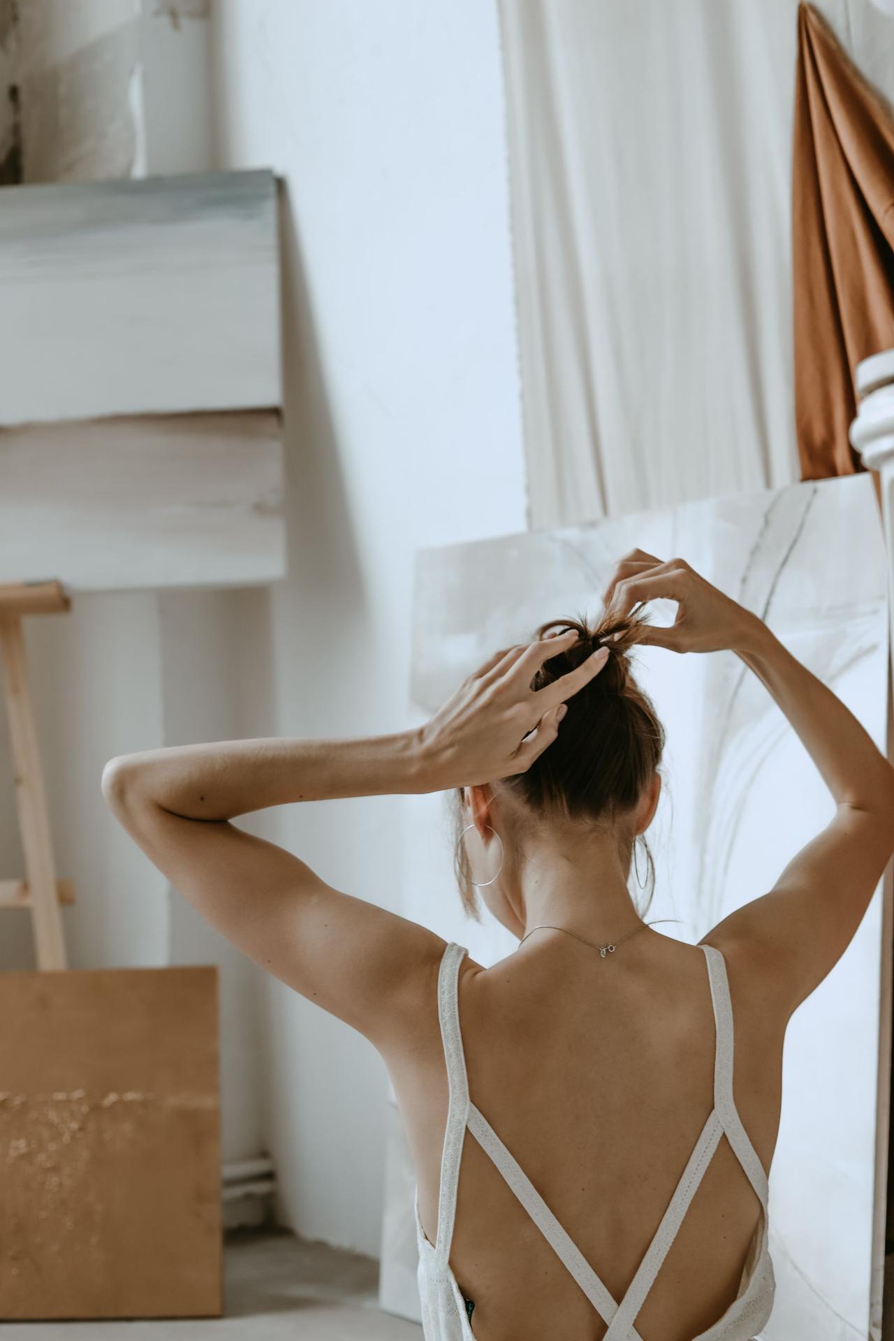 A woman adjusts her hair in a bright artistic studio, showcasing elegance and creativity.