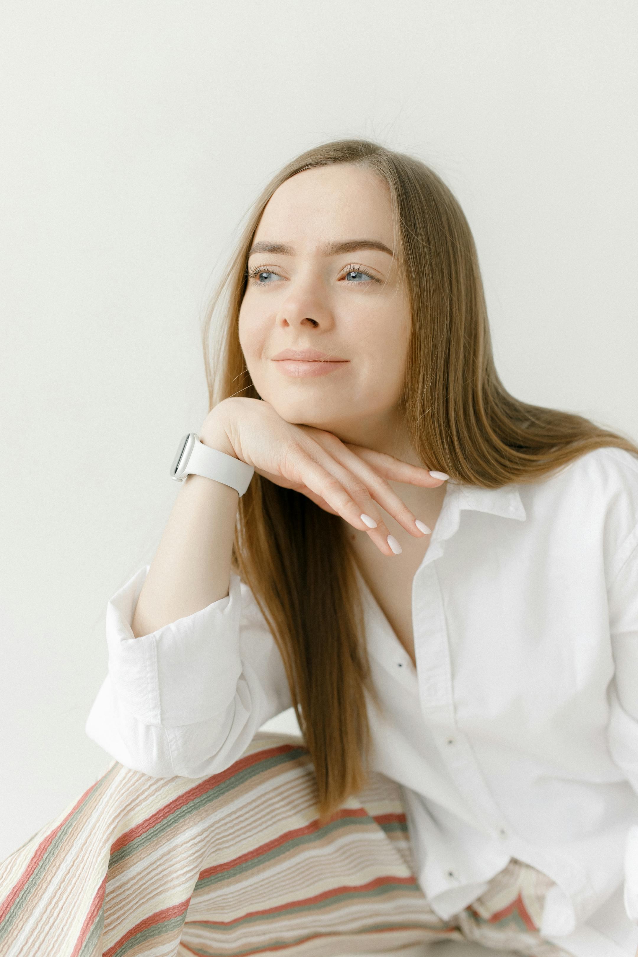 Young woman with hand on chin smiling in a studio with a white background.