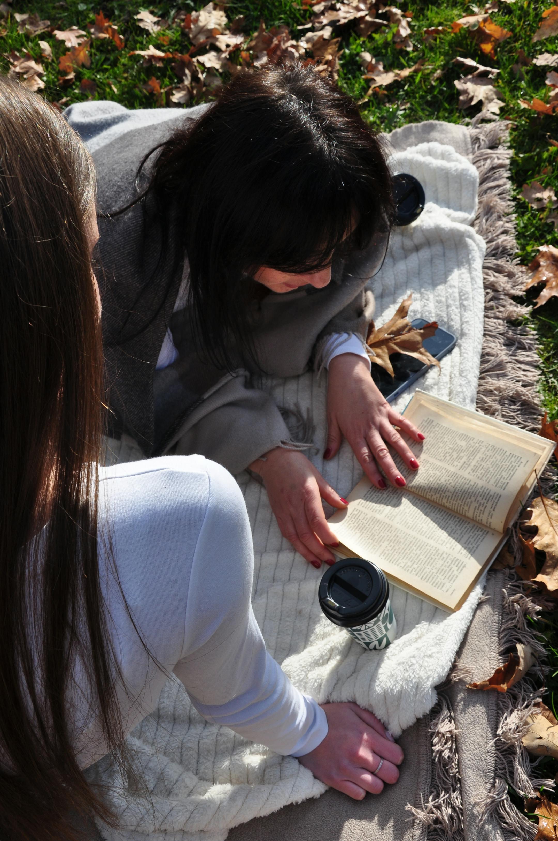 Two women enjoying a relaxing autumn picnic while reading a book outdoors.