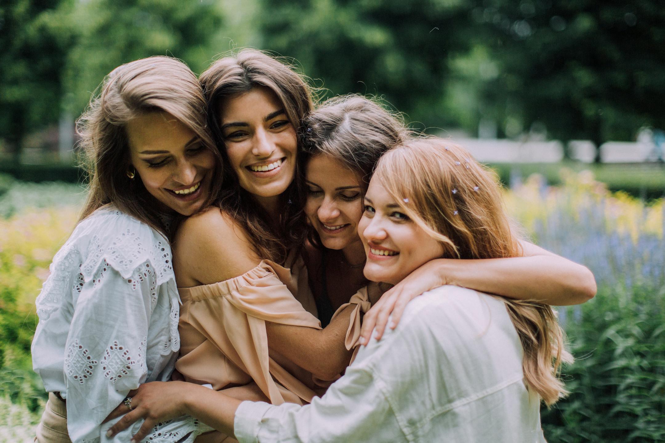 Four smiling women joyfully embrace in a lush green park during summer, showcasing genuine friendship and happiness.